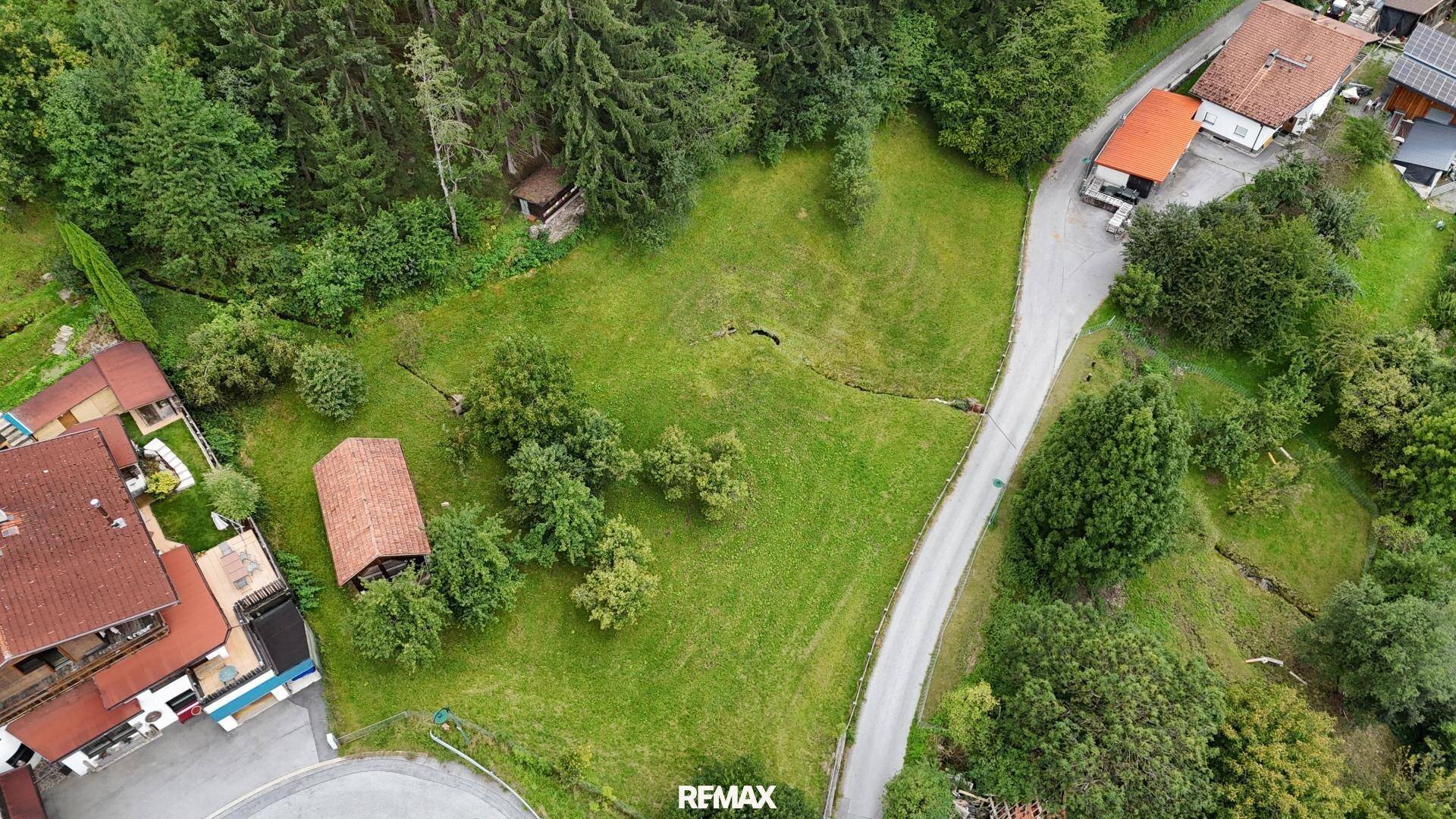 Luftaufnahme einer grünen Hügellandschaft mit verstreuten Häusern und dichtem Wald.