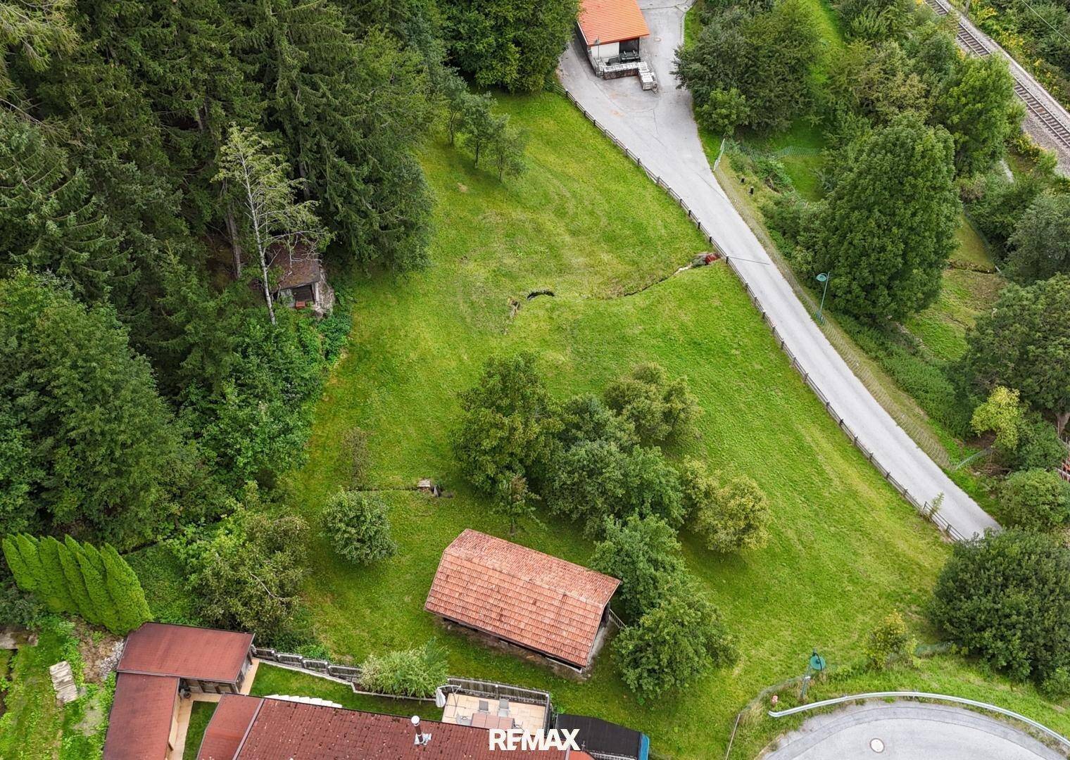 Luftaufnahme einer grünen, hügeligen Gegend mit Straße, einigen Häusern und dichtem Wald.