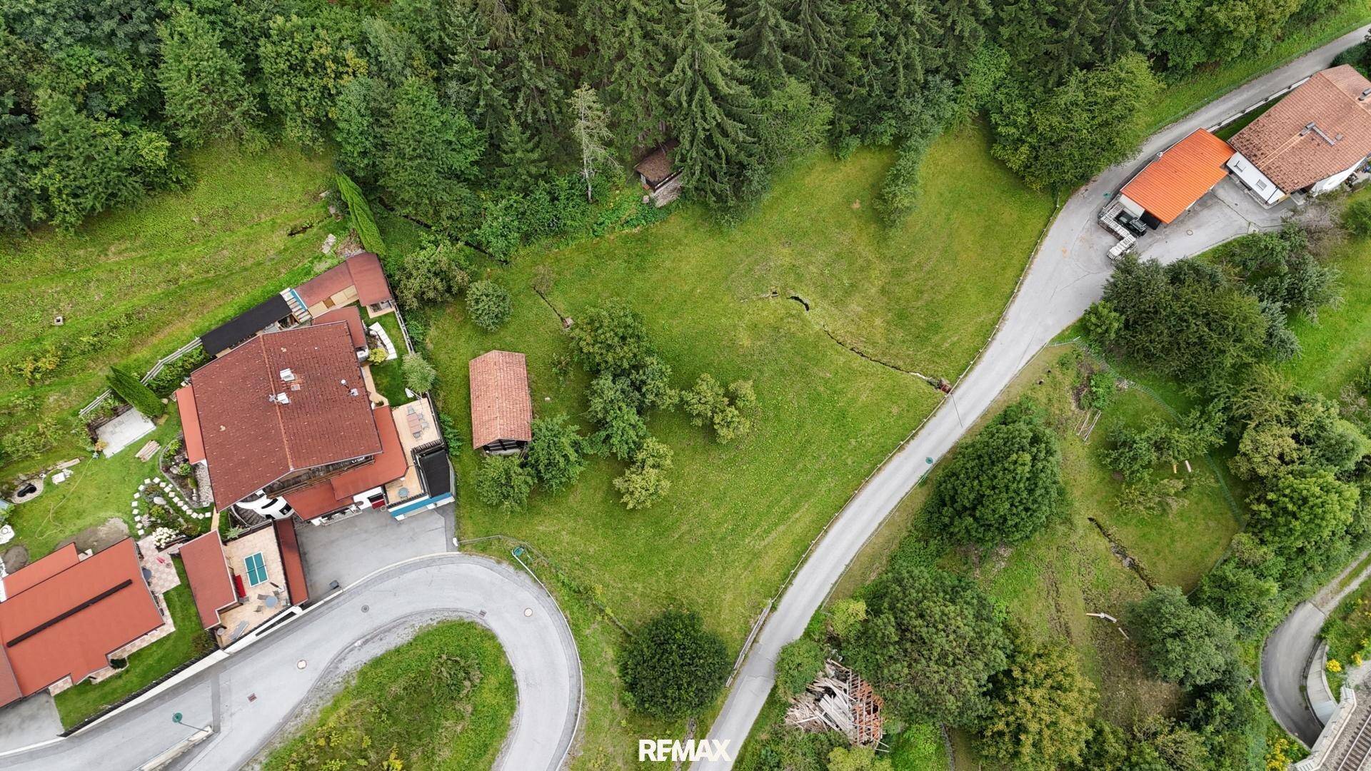 Luftaufnahme einer kurvenreichen Straße, Häusern mit roten Dächern, grünen Feldern und dichtem Wald.