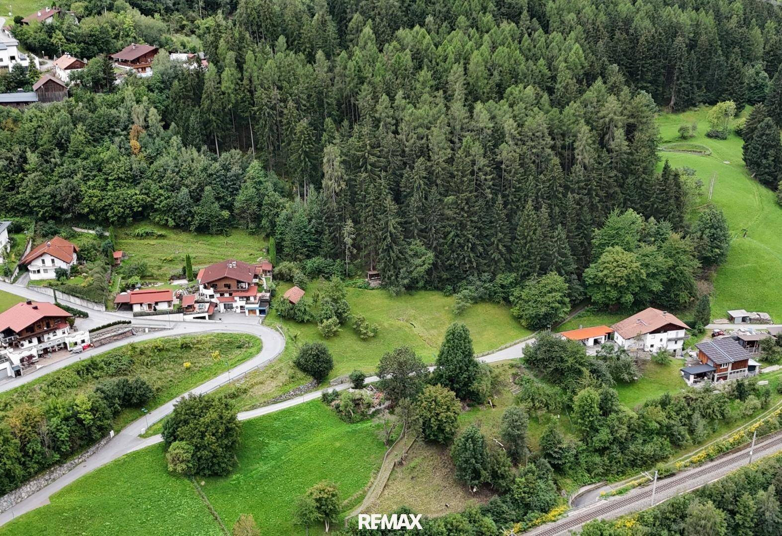 Luftaufnahme einer ländlichen Wohngegend mit Häusern, Straßen und dichtem Wald im Hintergrund.