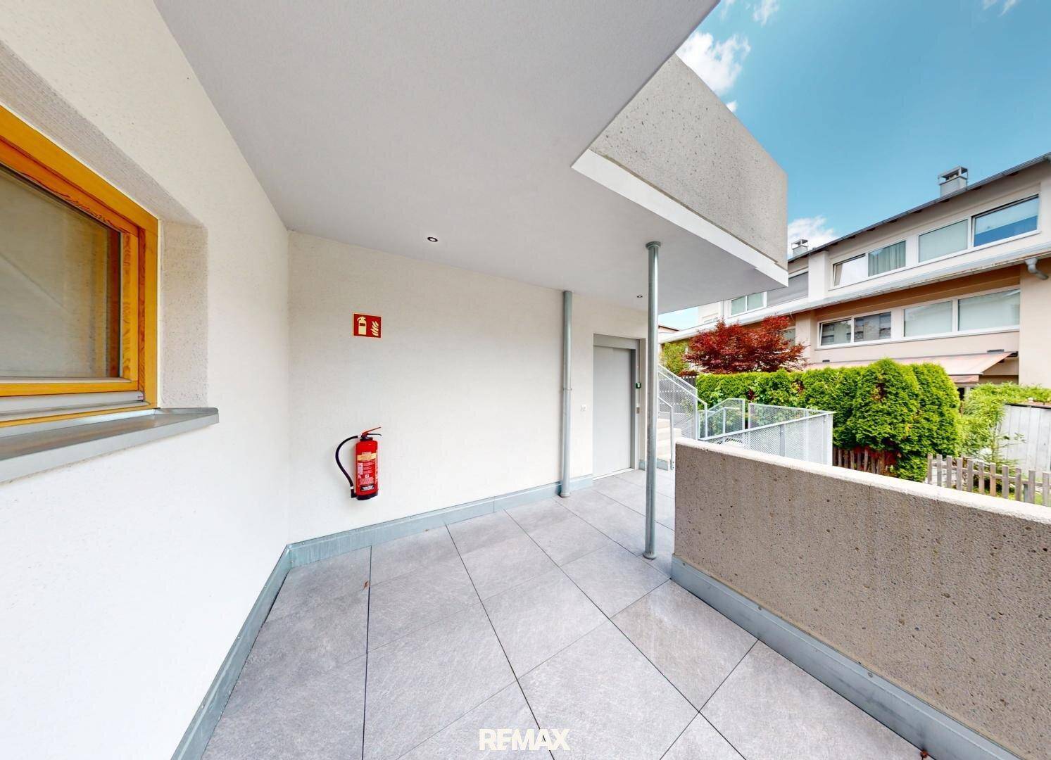 Überdachter Balkon mit Fliesenboden und Blick auf die umliegenden Häuser und Gärten.