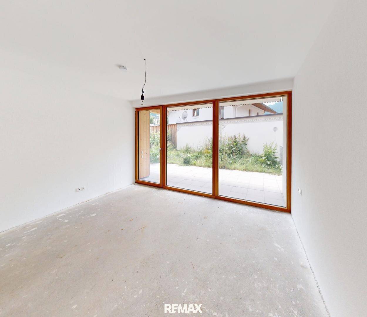 Heller, leerer Raum im Rohbau mit großen Fenstern und Zugang zum Außenbereich.