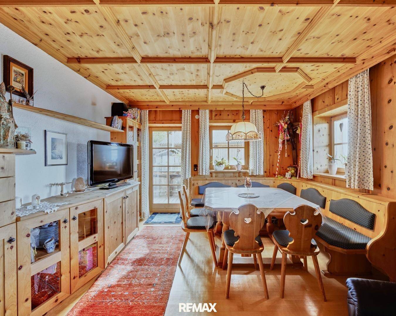 Geräumiger Wohn- und Essbereich im alpinen Stil mit Holzeinbauten und Zugang zum Balkon.