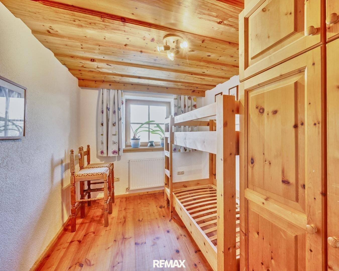 Kinderzimmer mit Etagenbett, Holzdecke und Holzboden, hell durch ein Fenster.