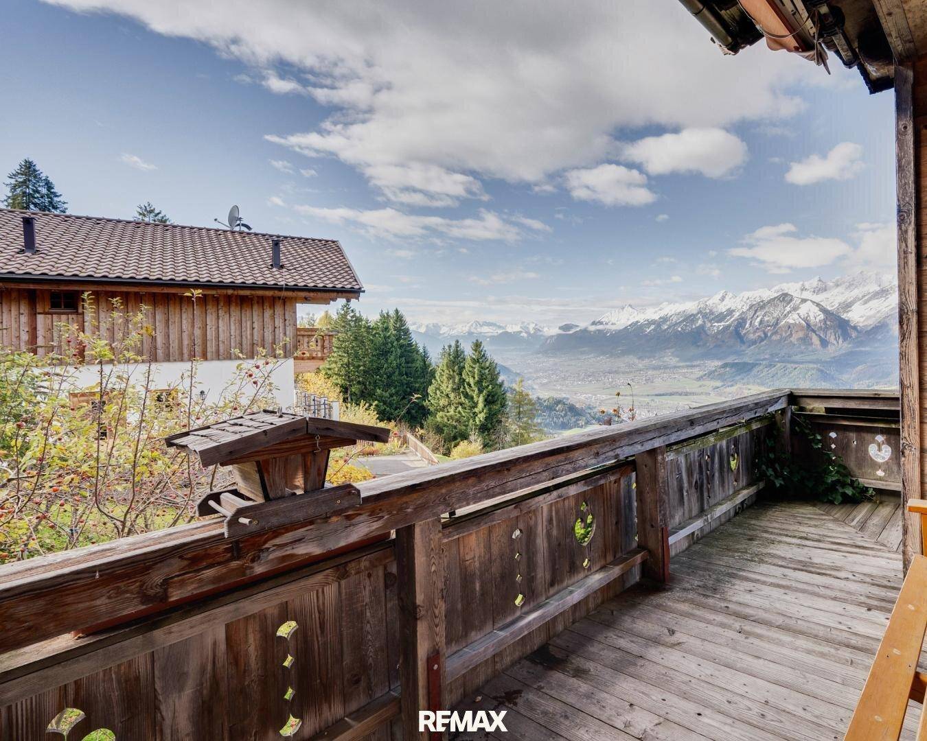 Rustikaler Holzbalkon mit traditionellem Geländer und weitem Blick auf die Berge.