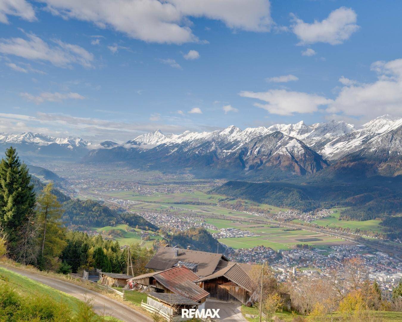 Panoramablick auf ein weites Tal mit schneebedeckten Bergen und grünen Landschaften.