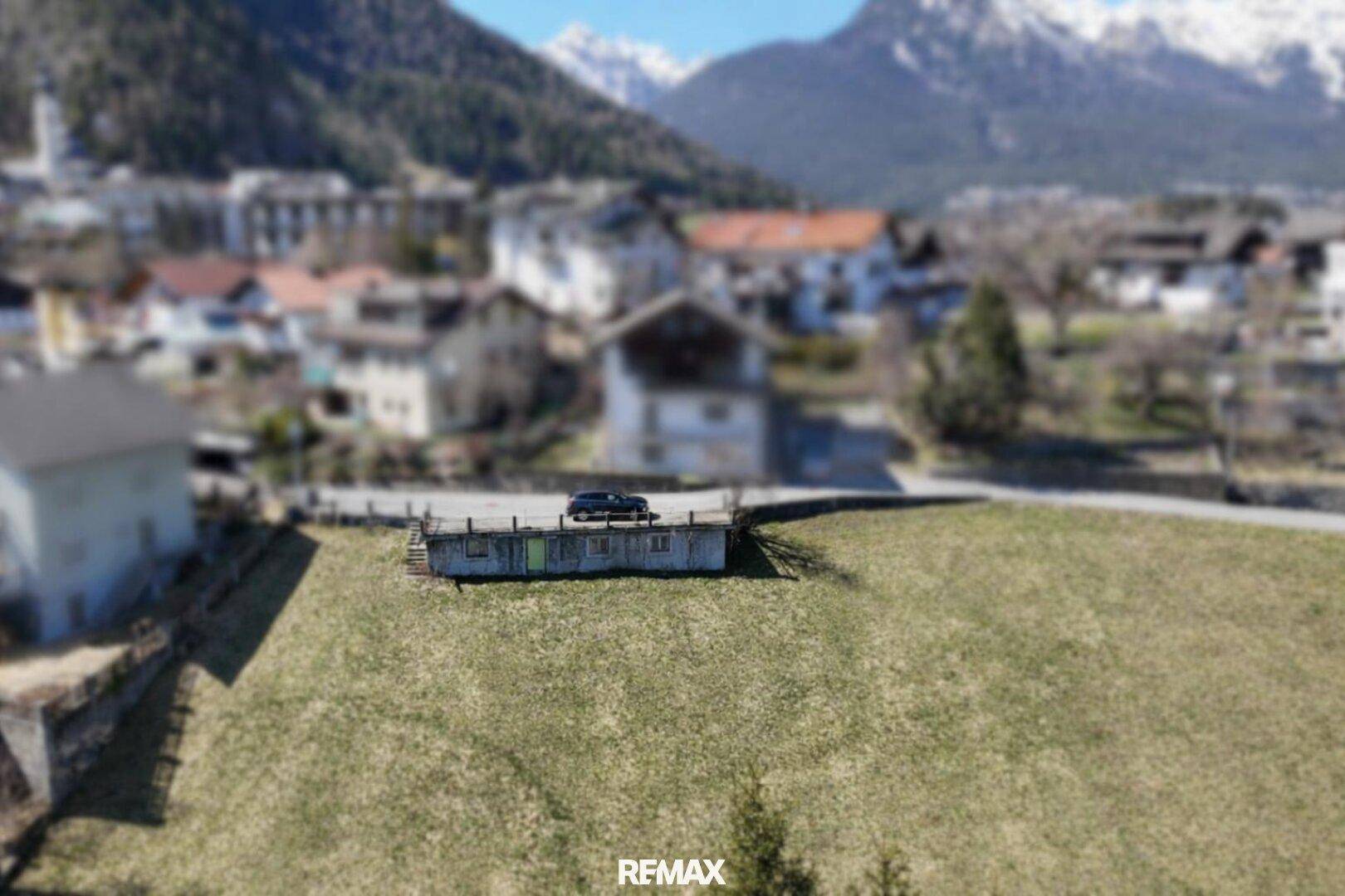 Übersicht über ein weitläufiges, grünes Grundstück mit einem kleinen Gebäude und einem Fahrzeug, mit Bergpanorama.