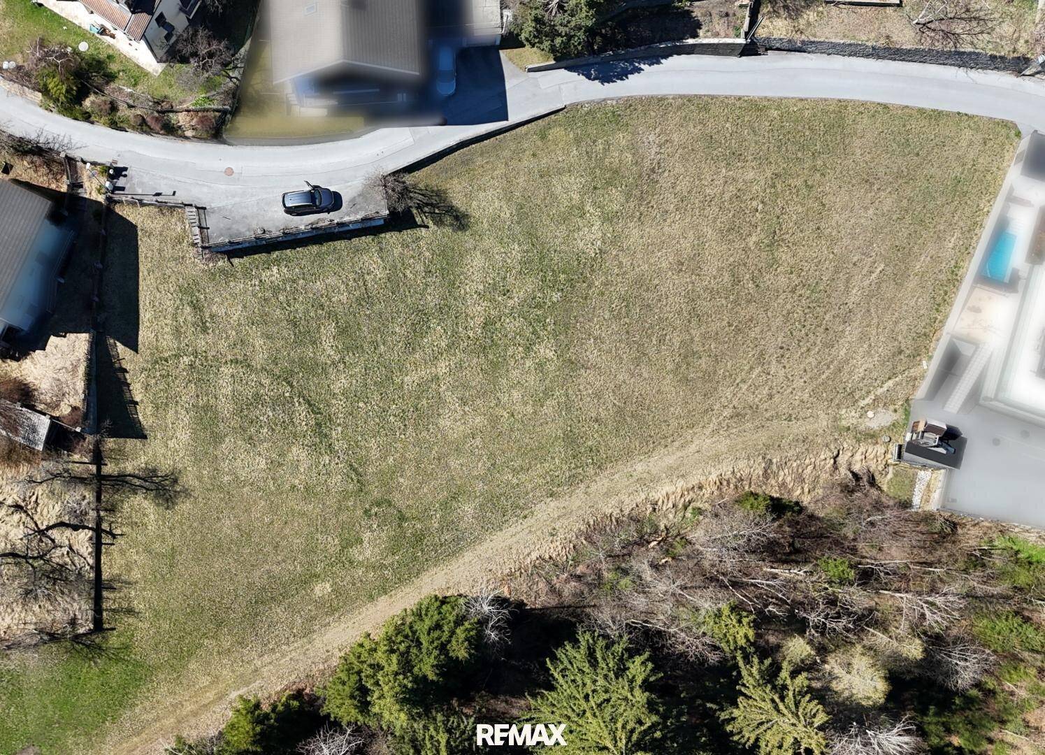 Vogelperspektive eines großen, unbebauten Grundstücks mit angrenzender Straße und umliegenden Häusern.