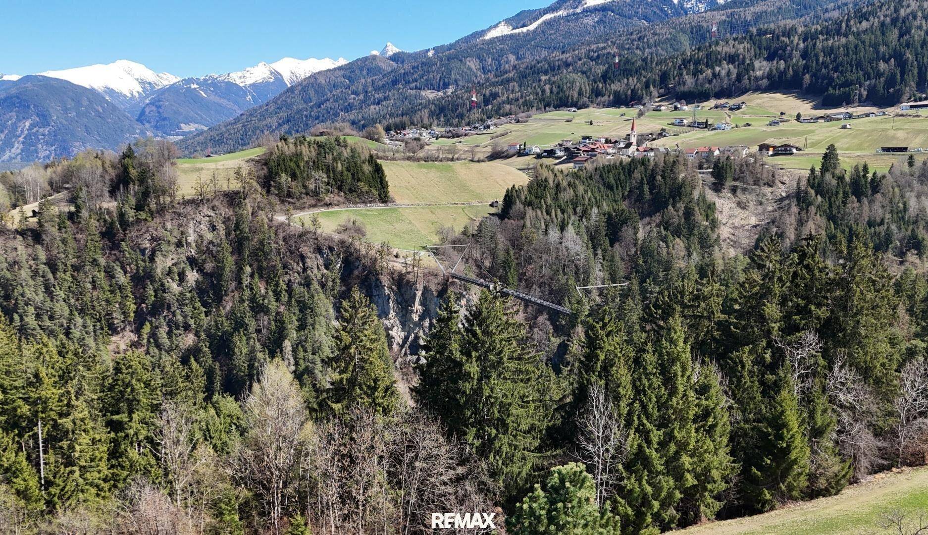Weitläufiger Panoramablick auf schneebedeckte Berge, grüne Täler und ein malerisches Dorf in der Ferne.