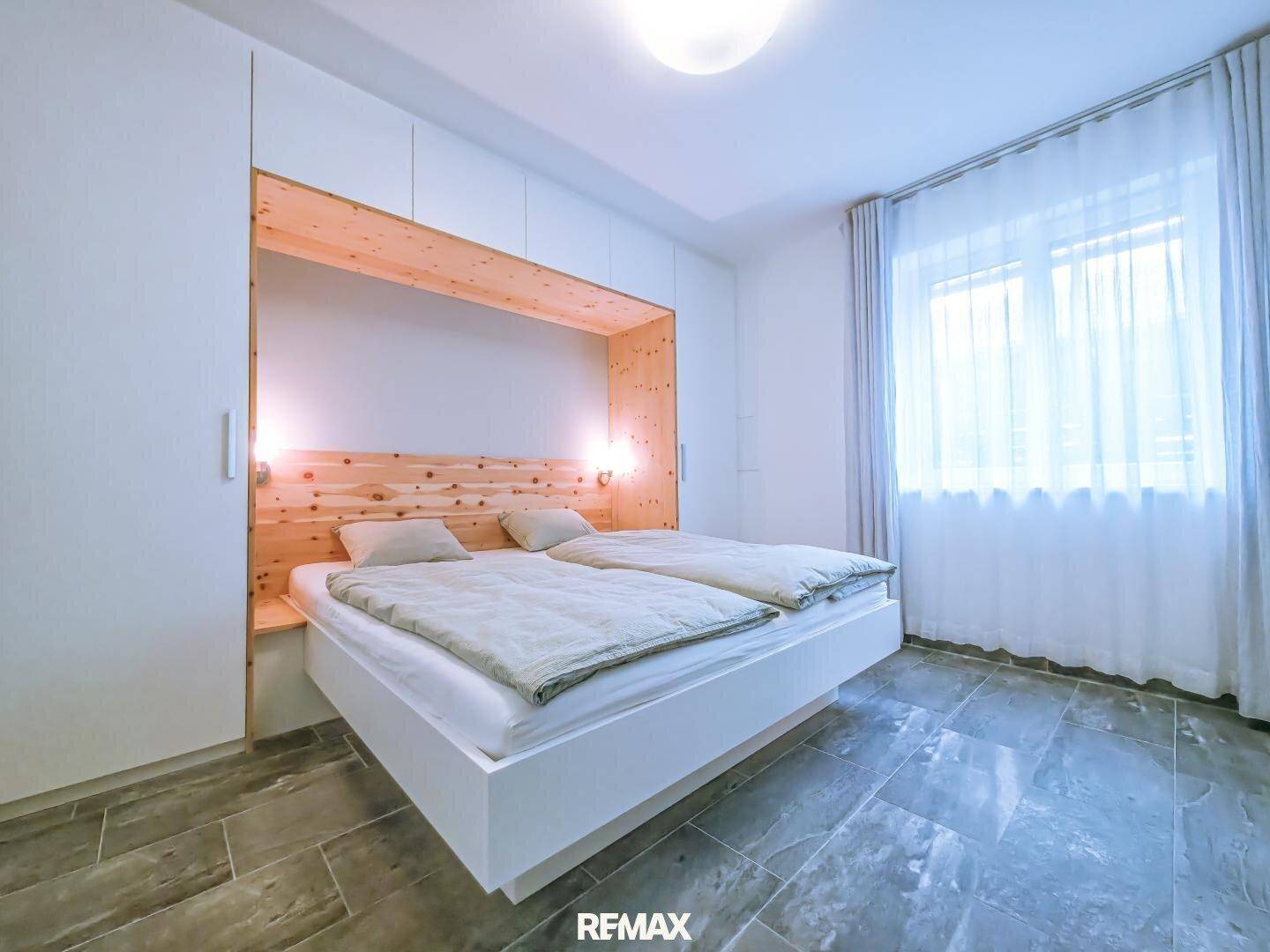 Modernes Schlafzimmer mit integriertem Holzbett, weißen Einbauschränken und großem Fenster für viel Tageslicht.