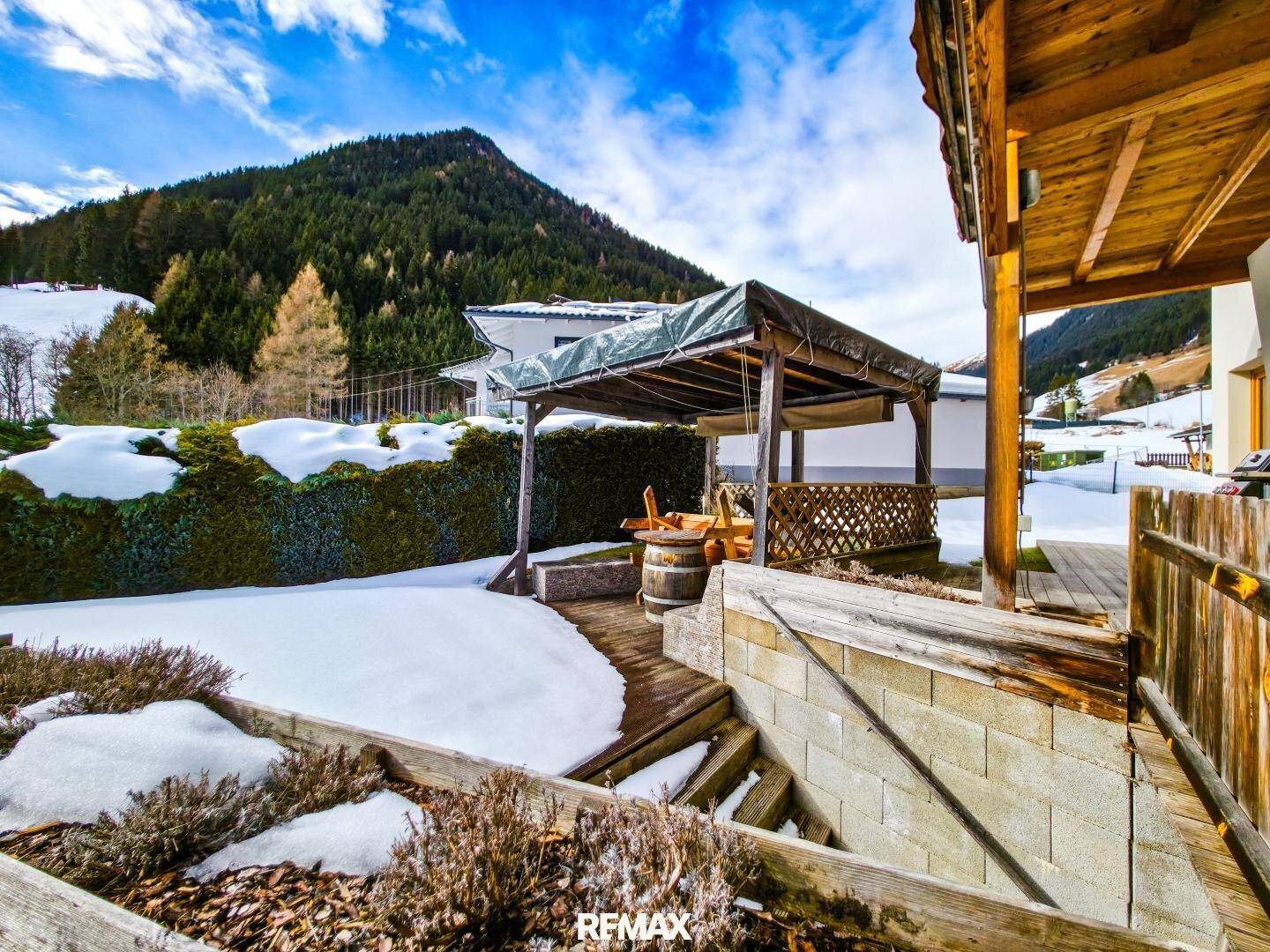 Außenbereich mit überdachtem Sitzplatz, Holzterrasse und verschneitem Garten.