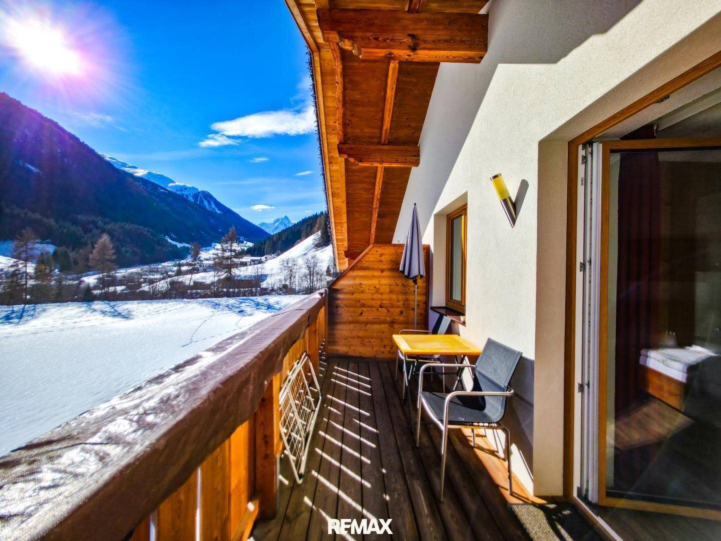 Sonniger Balkon mit Holzboden, Sitzgelegenheiten und atemberaubendem Bergblick.