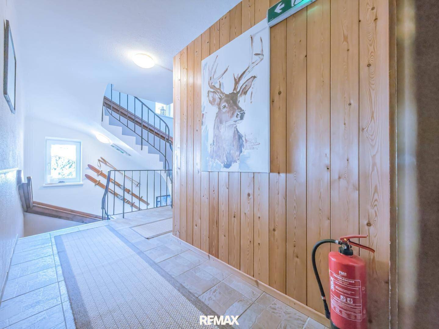 Treppenhaus mit Holzvertäfelung, Fliesenboden und einem Hirschgemälde an der Wand.