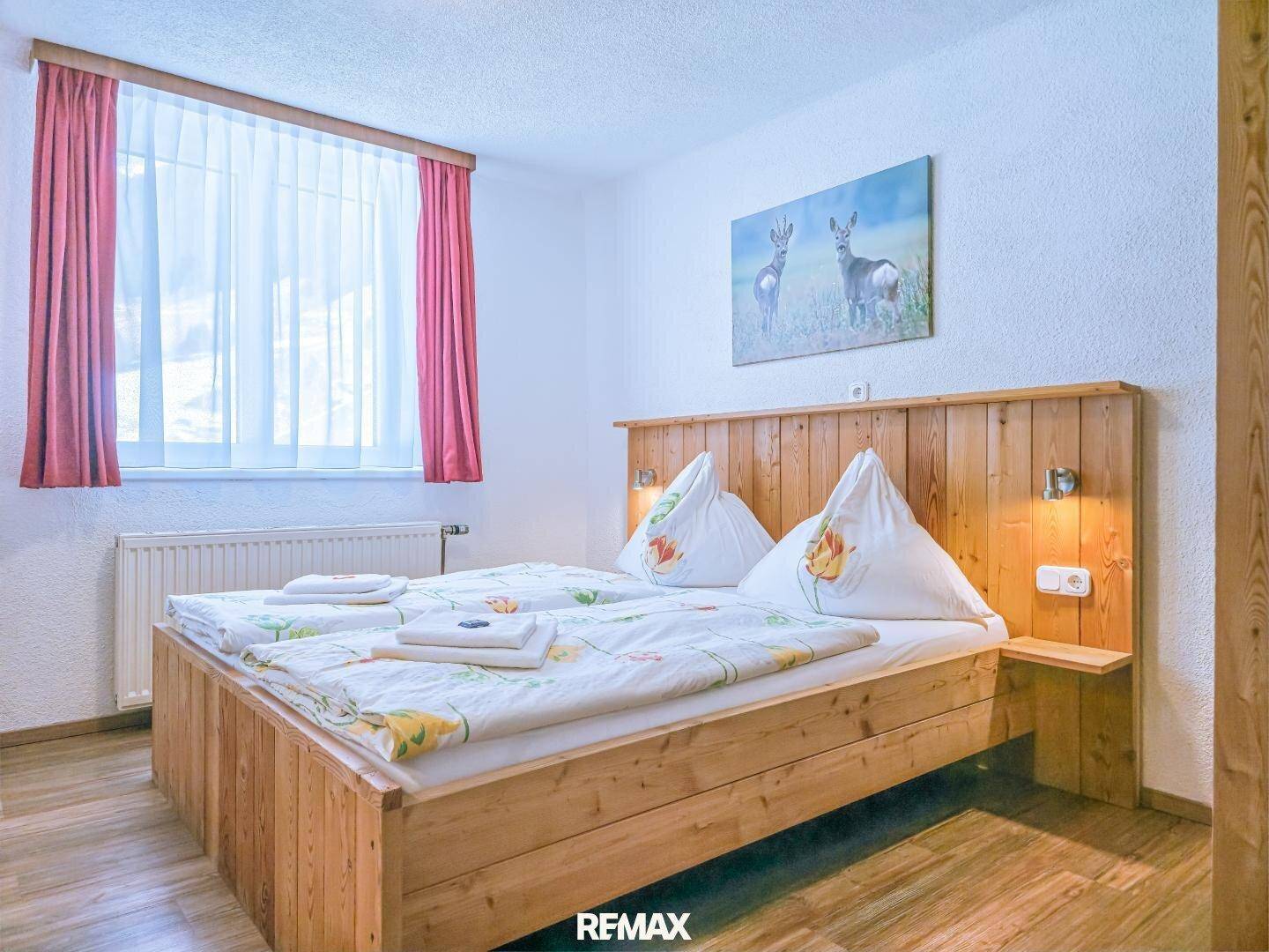 Helles Schlafzimmer mit Holzbett, großem Fenster und traditioneller Einrichtung.