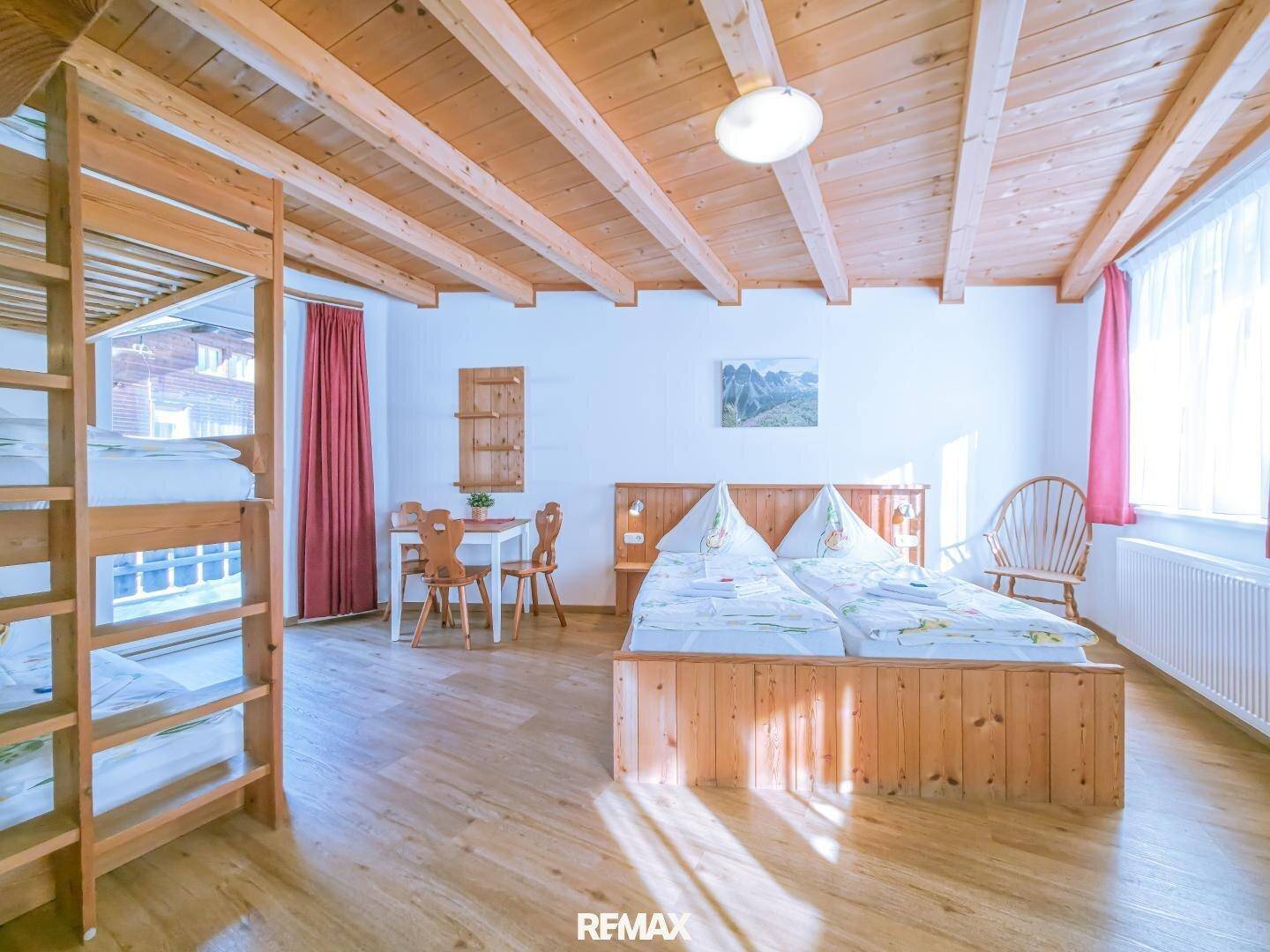 Geräumiges Schlafzimmer mit Doppelbett, Etagenbetten und sichtbaren Holzbalken an der Decke.