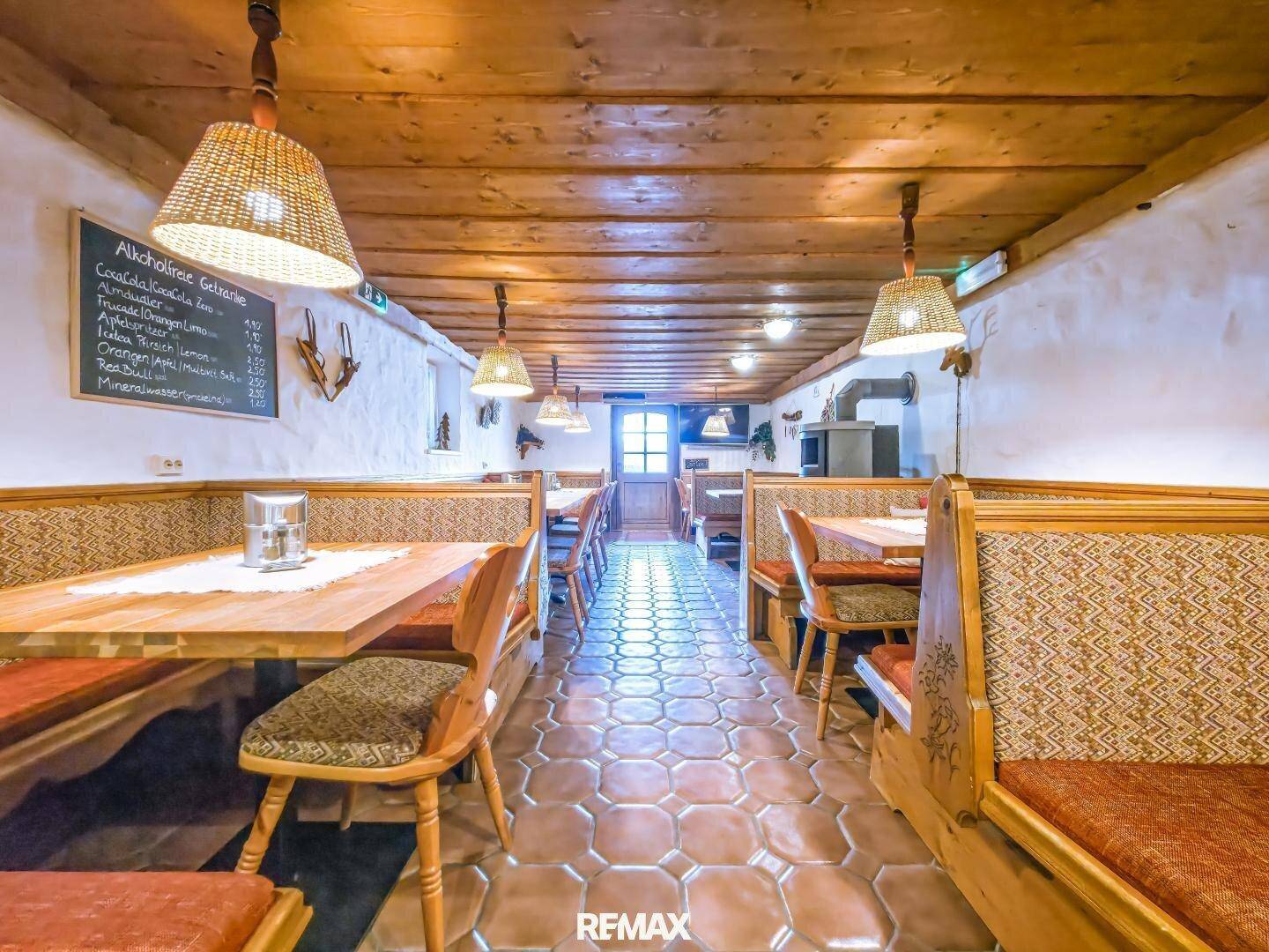 Traditioneller Restaurantbereich mit Holzbänken, Tischen und rustikalen Deckenbalken.