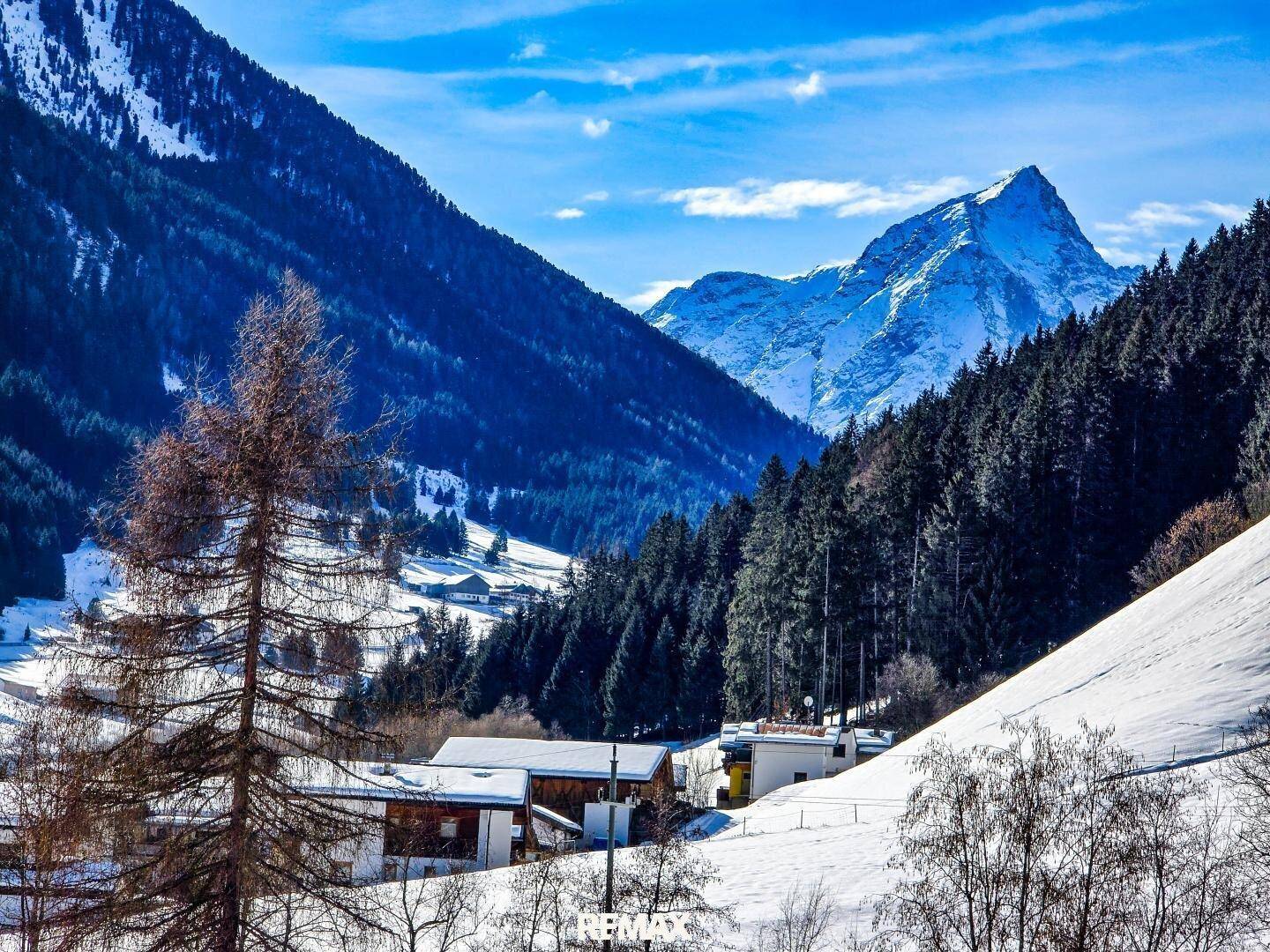 Malerische Berglandschaft mit schneebedeckten Gipfeln, Wäldern und blauem Himmel.