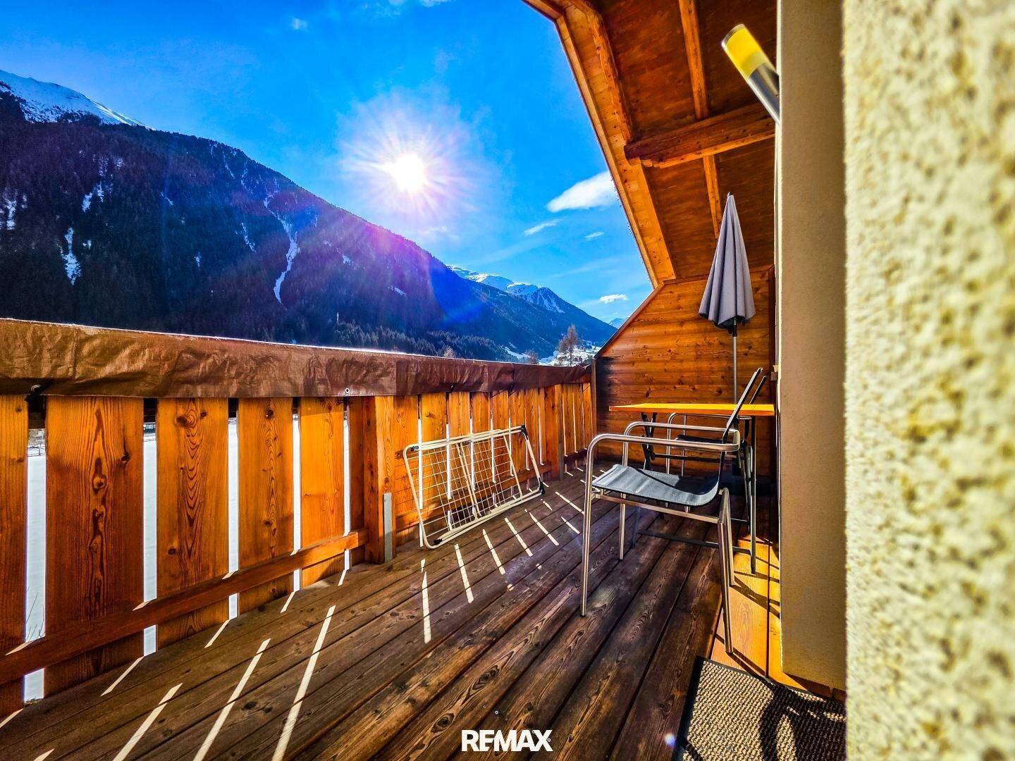 Gemütlicher Balkon mit Holzboden, Sonnenschirm und weitem Blick auf die Berge.