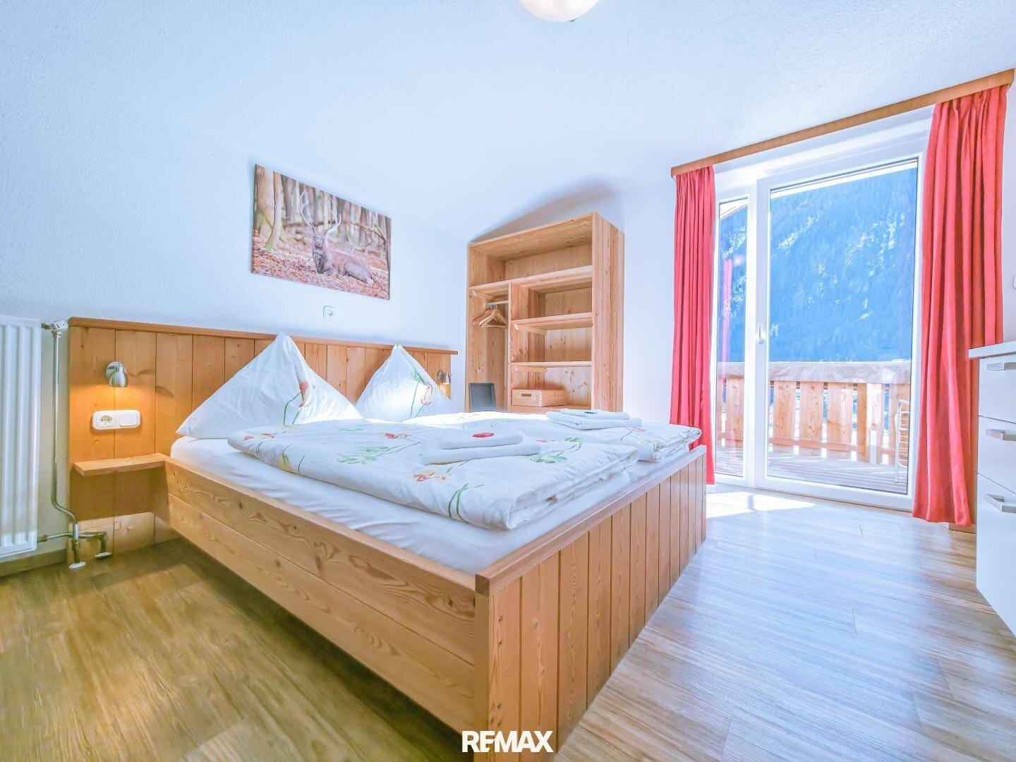 Komfortables Schlafzimmer mit Holzbett, offenem Kleiderschrank und Zugang zum Balkon.