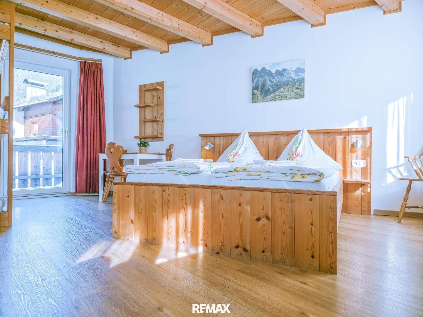 Gemütliches Schlafzimmer mit Holzbalkendecke, Doppelbett und Zugang zu einem Balkon.