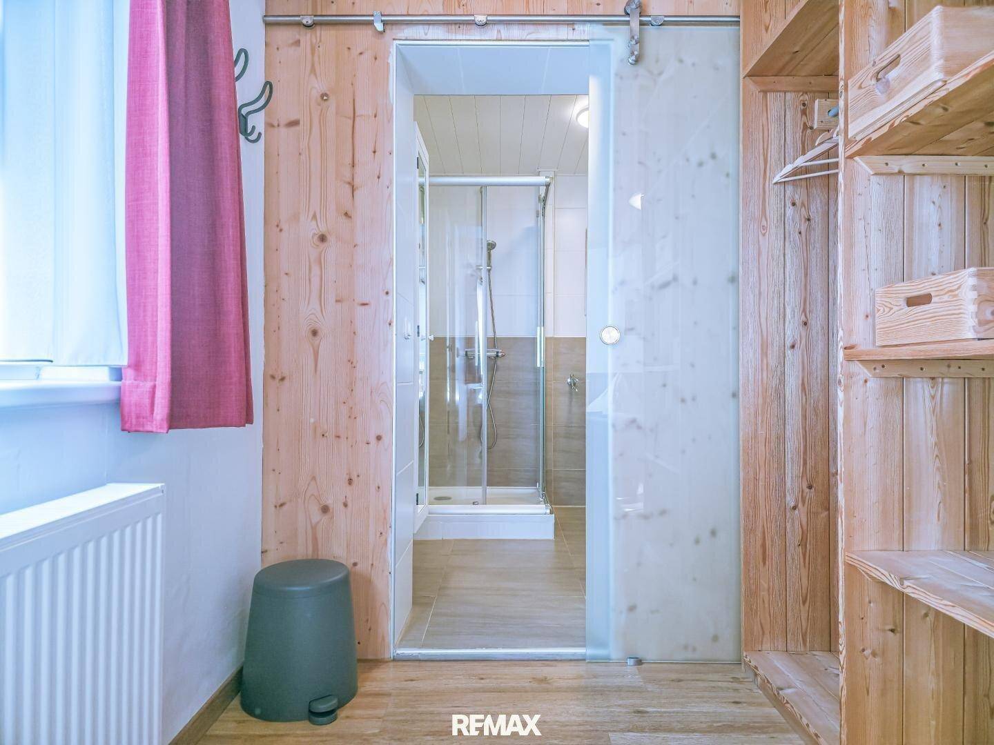 Schlafzimmer mit offenem Kleiderschrank und Blick durch eine Glastür in ein Badezimmer.