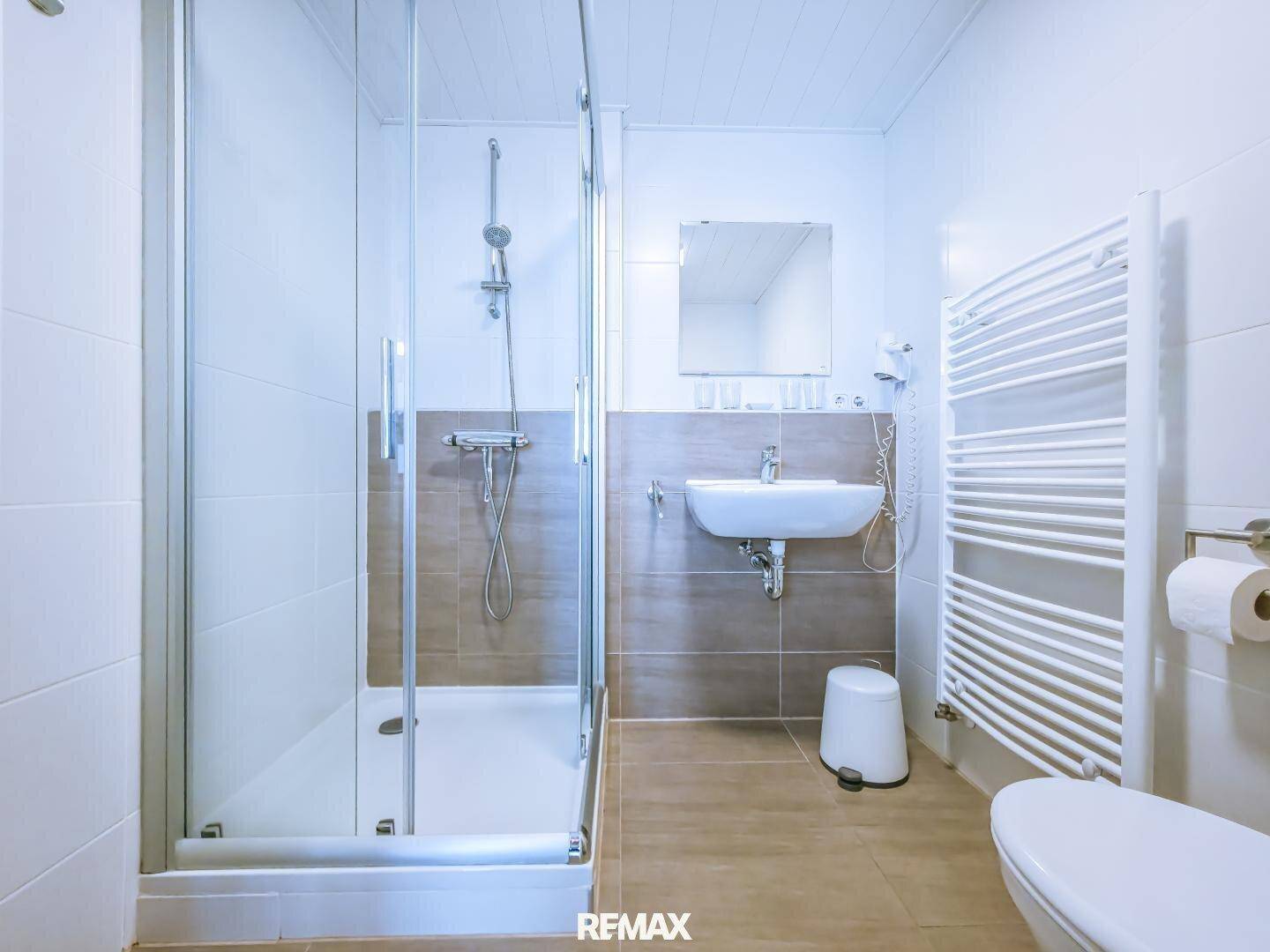 Helles Badezimmer mit Duschkabine, Waschbecken und einem praktischen Handtuchheizkörper.