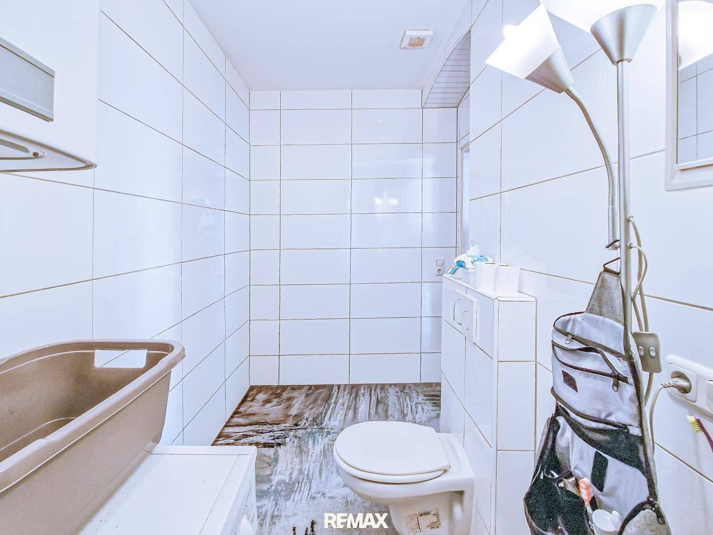Gefliestes Badezimmer mit Toilette und einem Boden, der auf eine Duschzone hindeutet.