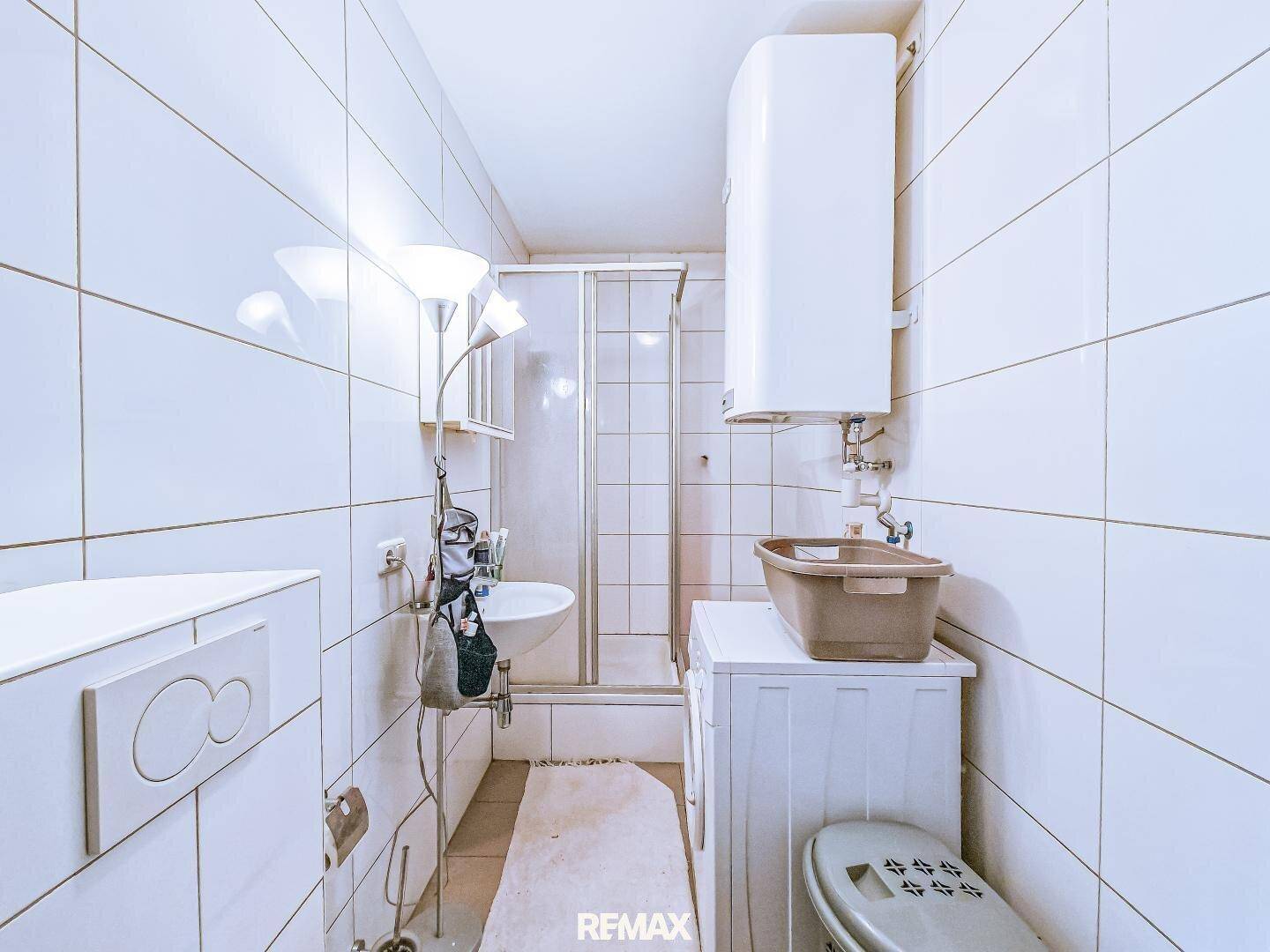 Helles, gefliestes Badezimmer mit Duschkabine, Waschbecken und Toilette.