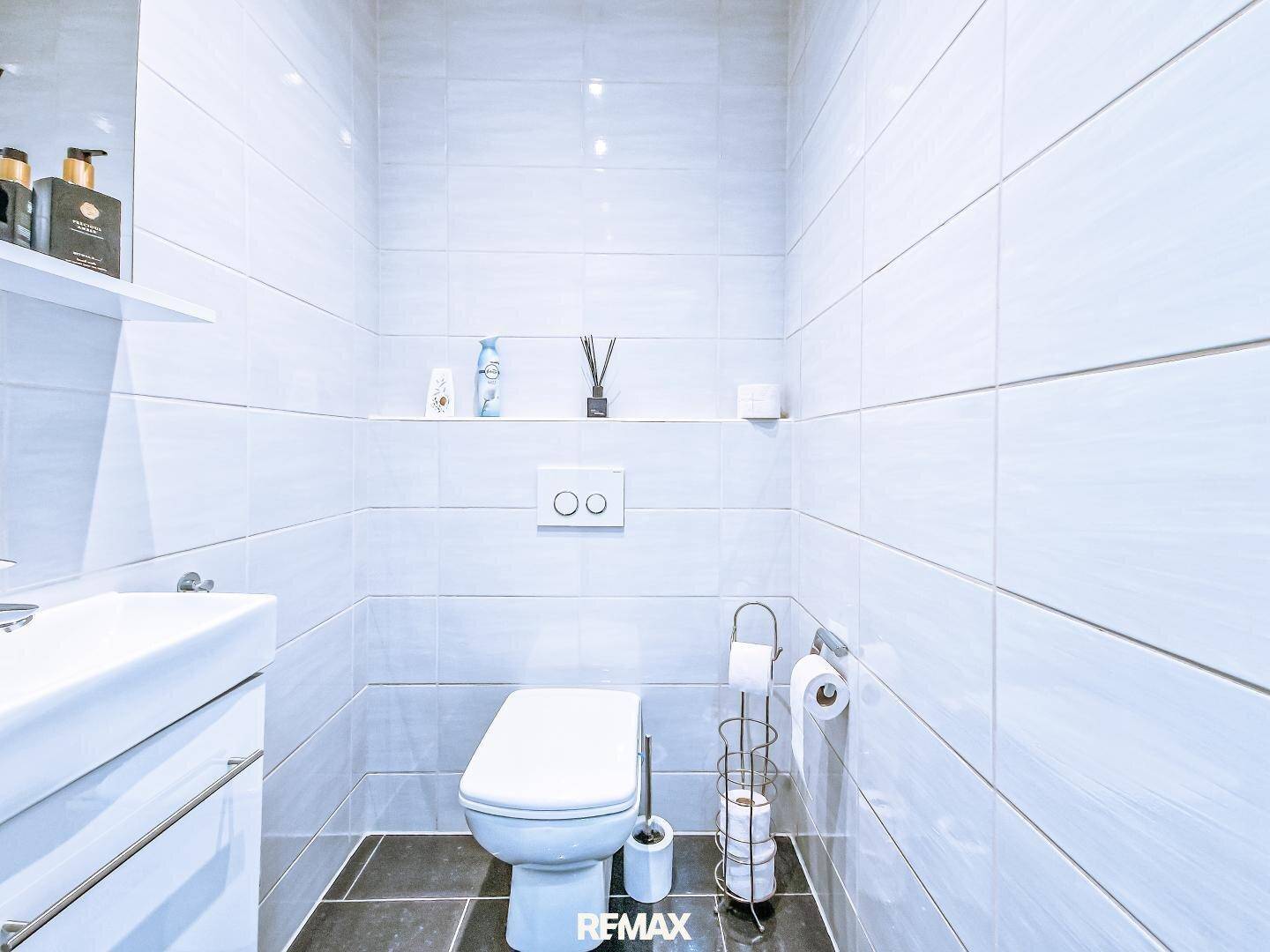 Modernes Gäste-WC mit weißen Wandfliesen, dunklem Boden und wandhängendem WC.
