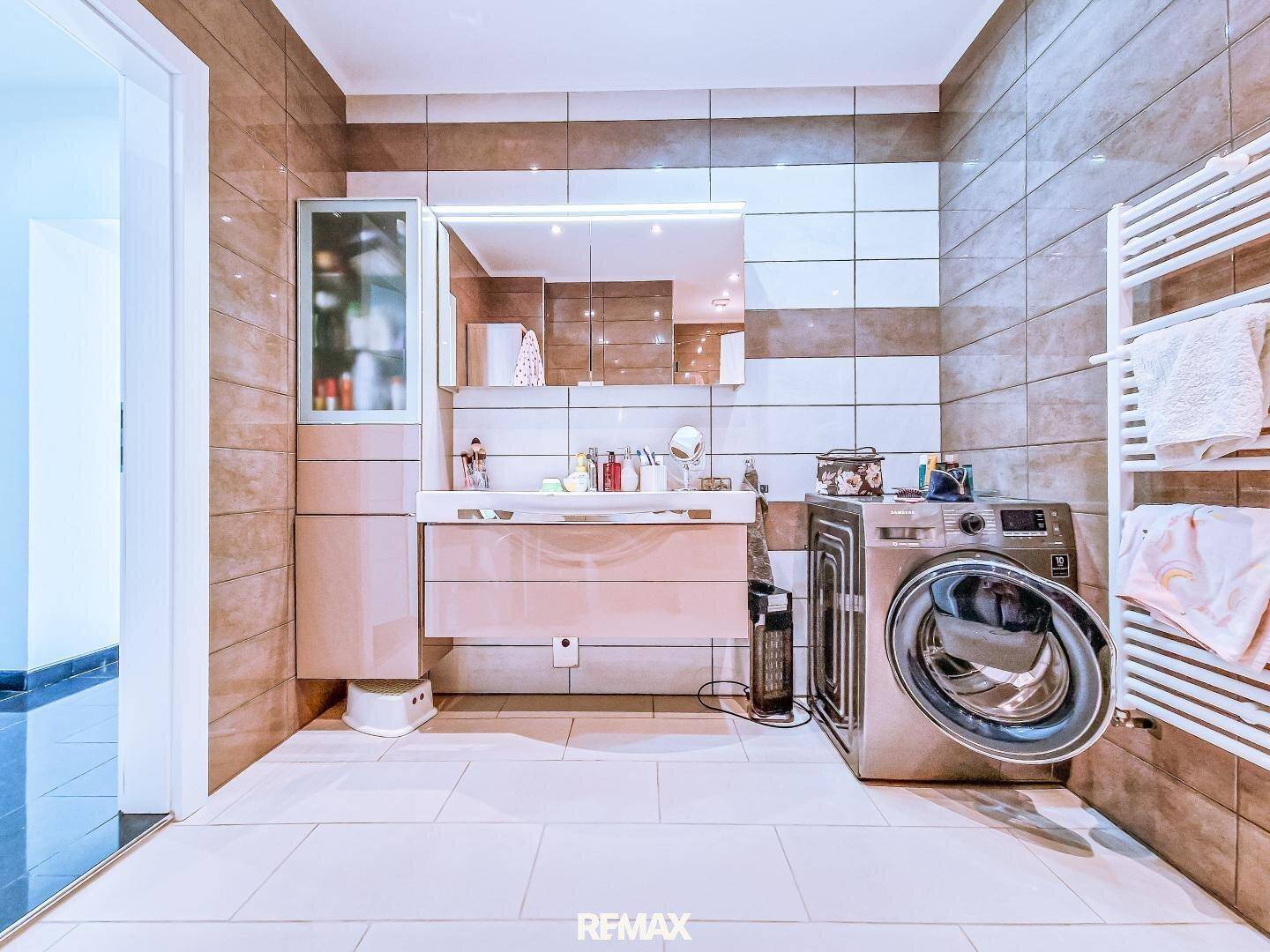 Modernes Badezimmer mit Waschtisch, Spiegelschrank, Waschmaschine und braunen Fliesen.