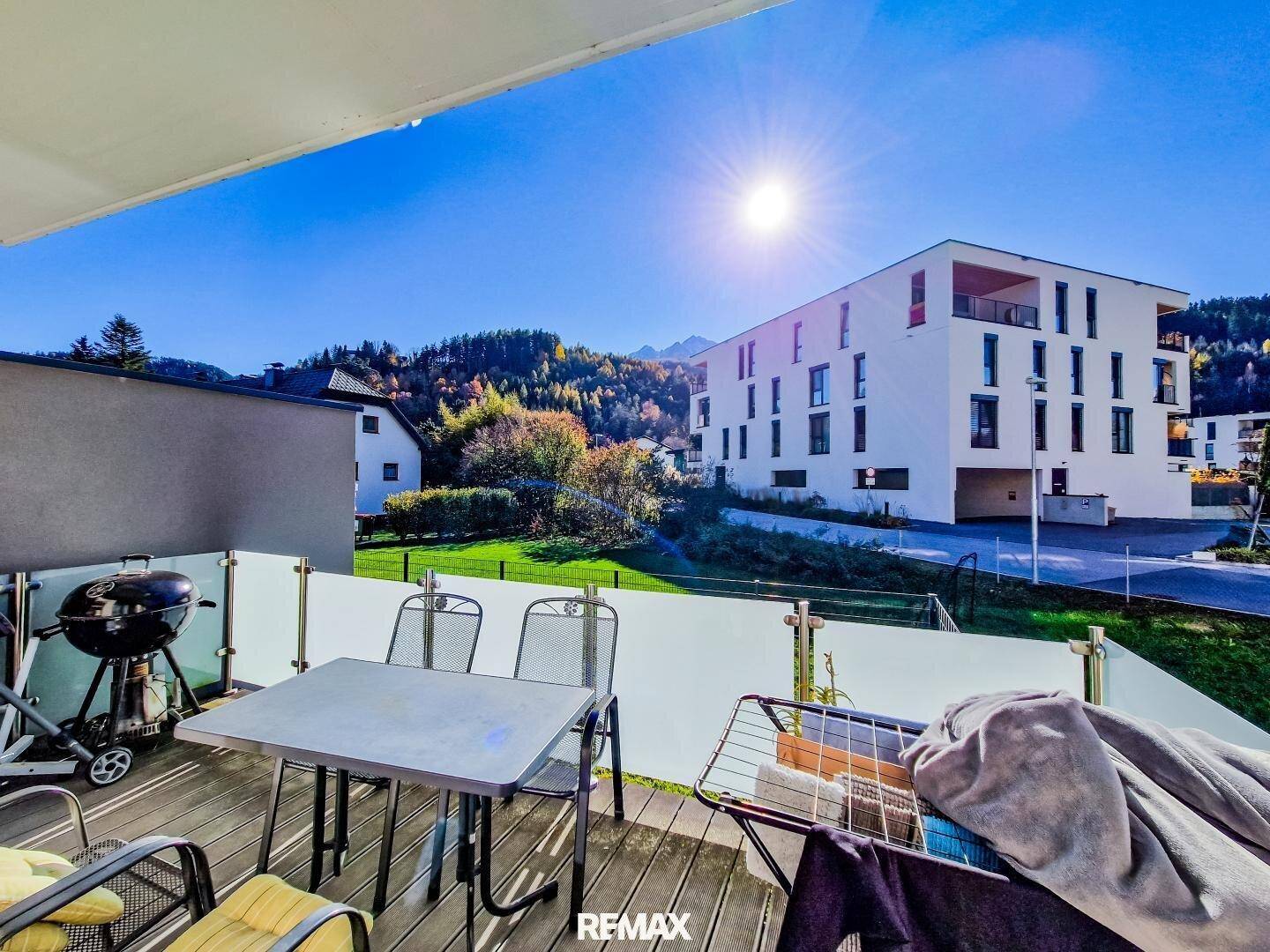 Sonniger Balkon mit Esstisch und weitem Blick auf moderne Gebäude und Berge.