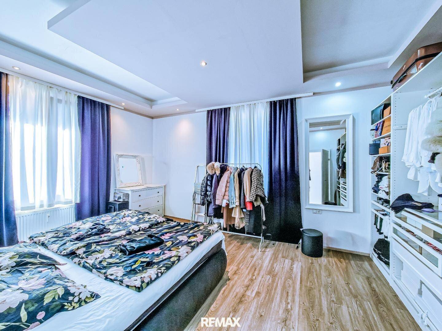 Schlafzimmer mit großem Bett, floraler Bettwäsche und offenem Kleiderschranksystem.