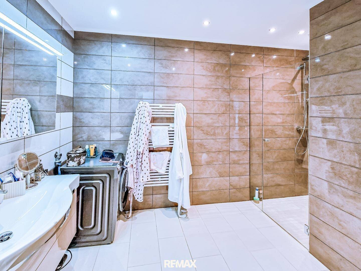 Geräumiges Badezimmer mit begehbarer Dusche, Waschmaschine und beheiztem Handtuchhalter.