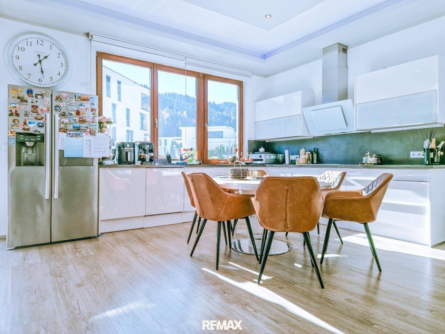 Moderne weiße Küche mit Essbereich, großem Fenster und viel Tageslicht.