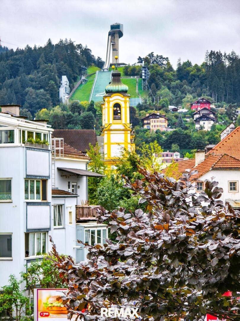 Panoramablick auf die Stadt mit Kirche und Skisprungschanze im Hintergrund.