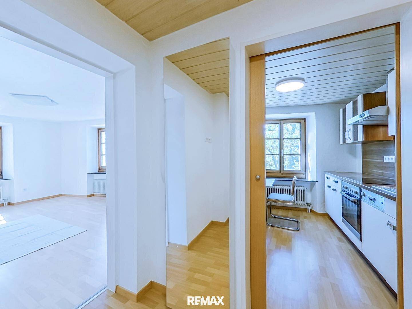 Heller Flur mit Holzboden, der zu einer Küche und einem weiteren Zimmer führt.