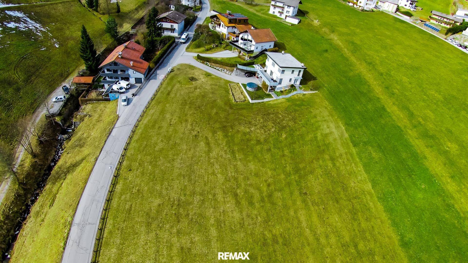 Luftaufnahme eines weitläufigen grünen Grundstücks mit angrenzender Straße und Häusern.