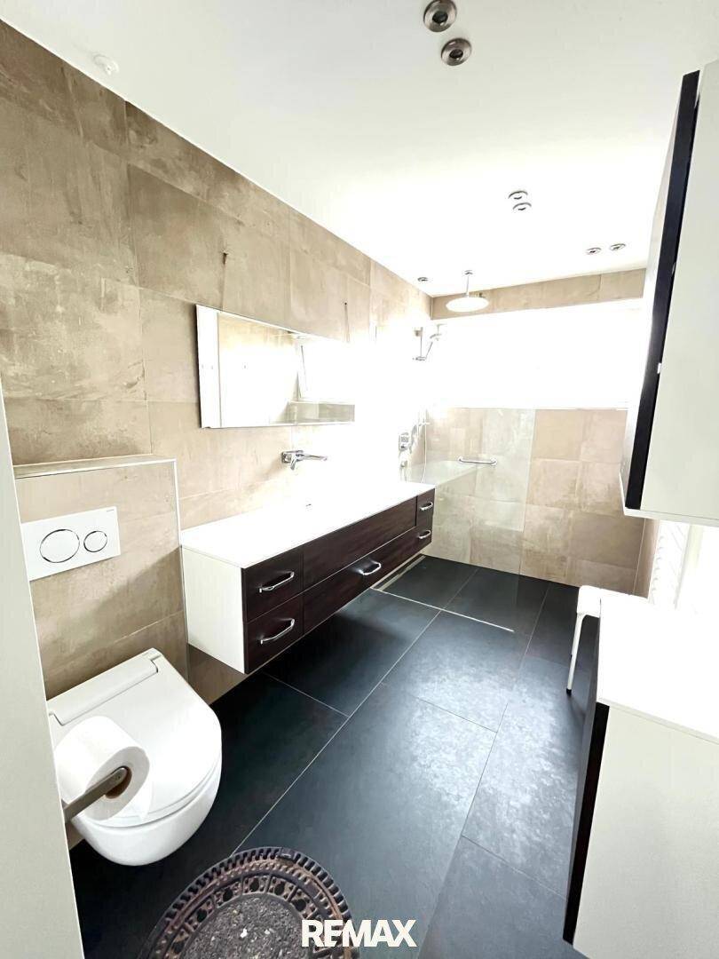 Modernes Badezimmer mit großen Fliesen, schwebendem Waschtisch und wandhängendem WC.