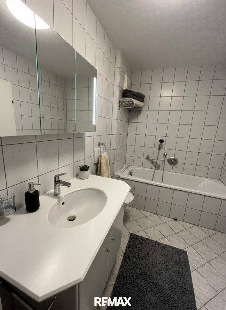 Badezimmer mit Badewanne, Einzelwaschbecken und weiß gefliesten Wänden und Boden.