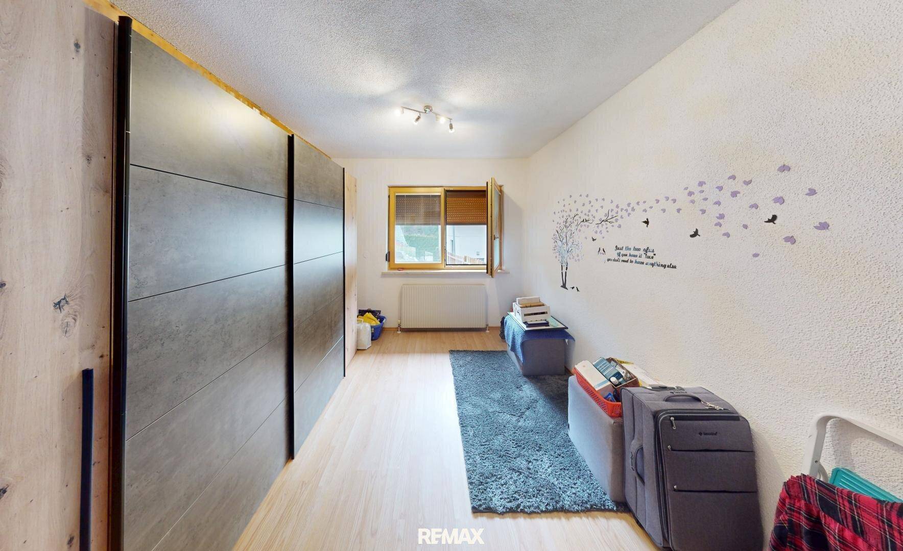 Schlafzimmer mit großem Einbauschrank, hellem Boden und Fenster mit Blick nach draußen.