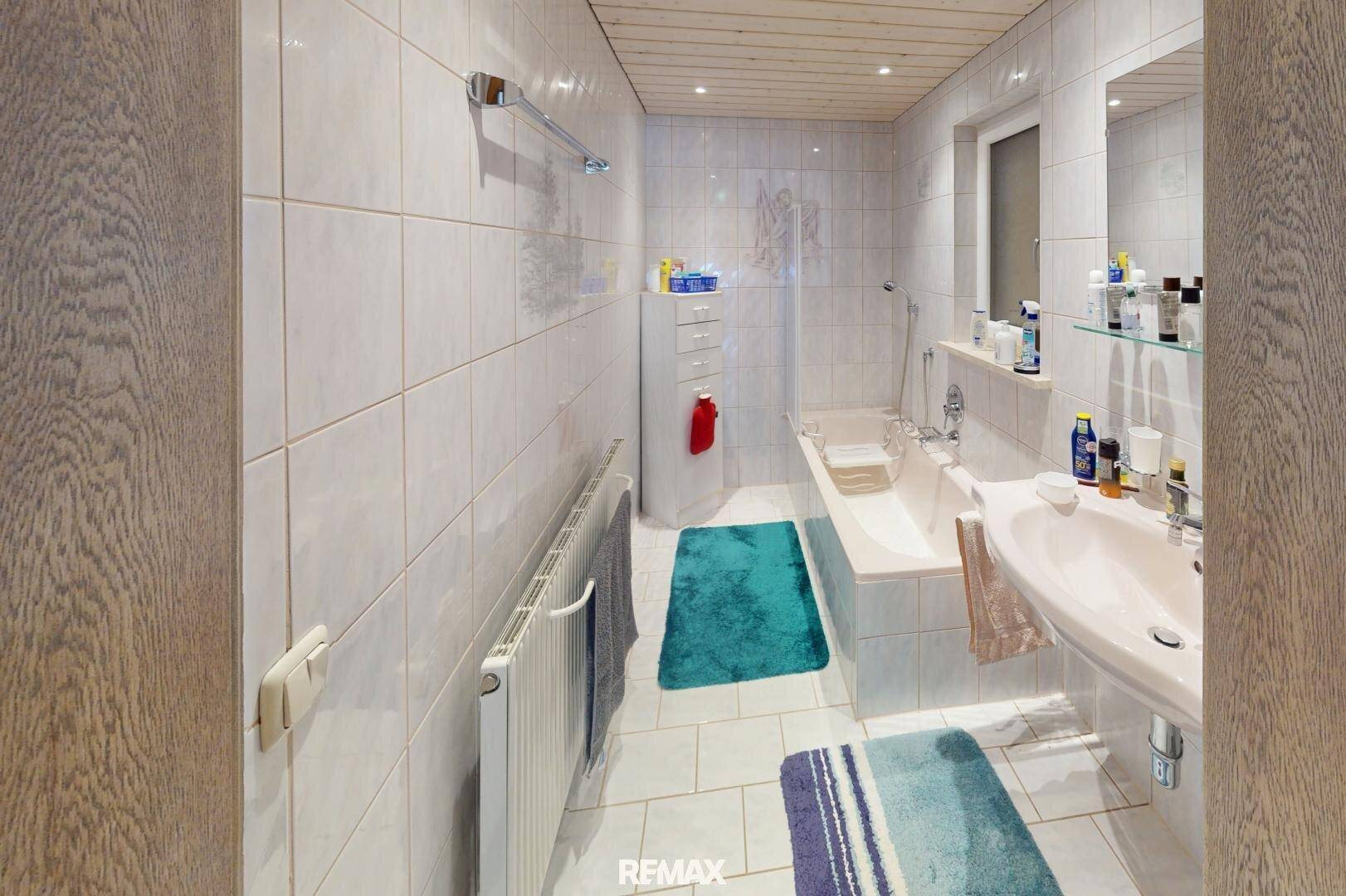 Badezimmer mit weißen Fliesen, Badewanne, Waschbecken und Holzdecke.