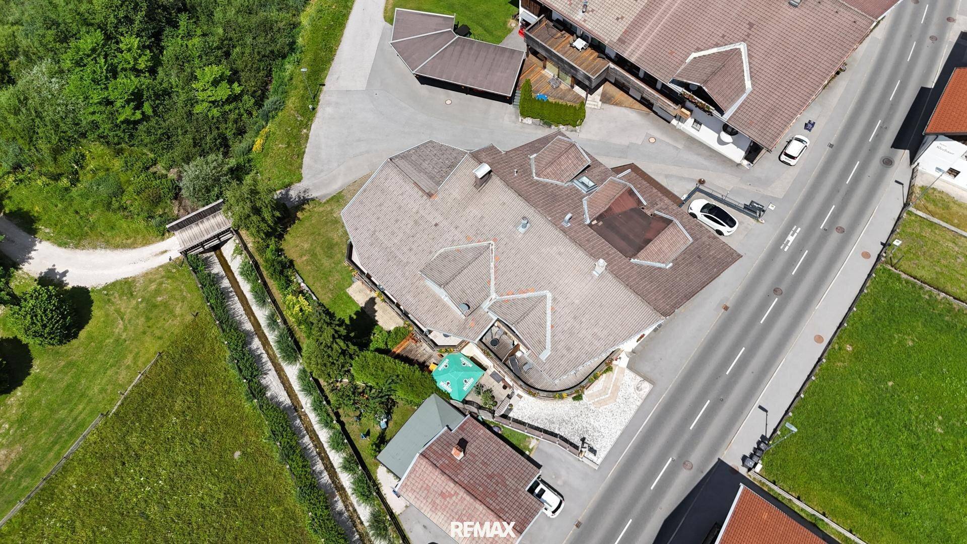 Luftaufnahme eines Gebäudekomplexes mit Satteldächern und umliegenden Straßen und Grünflächen.