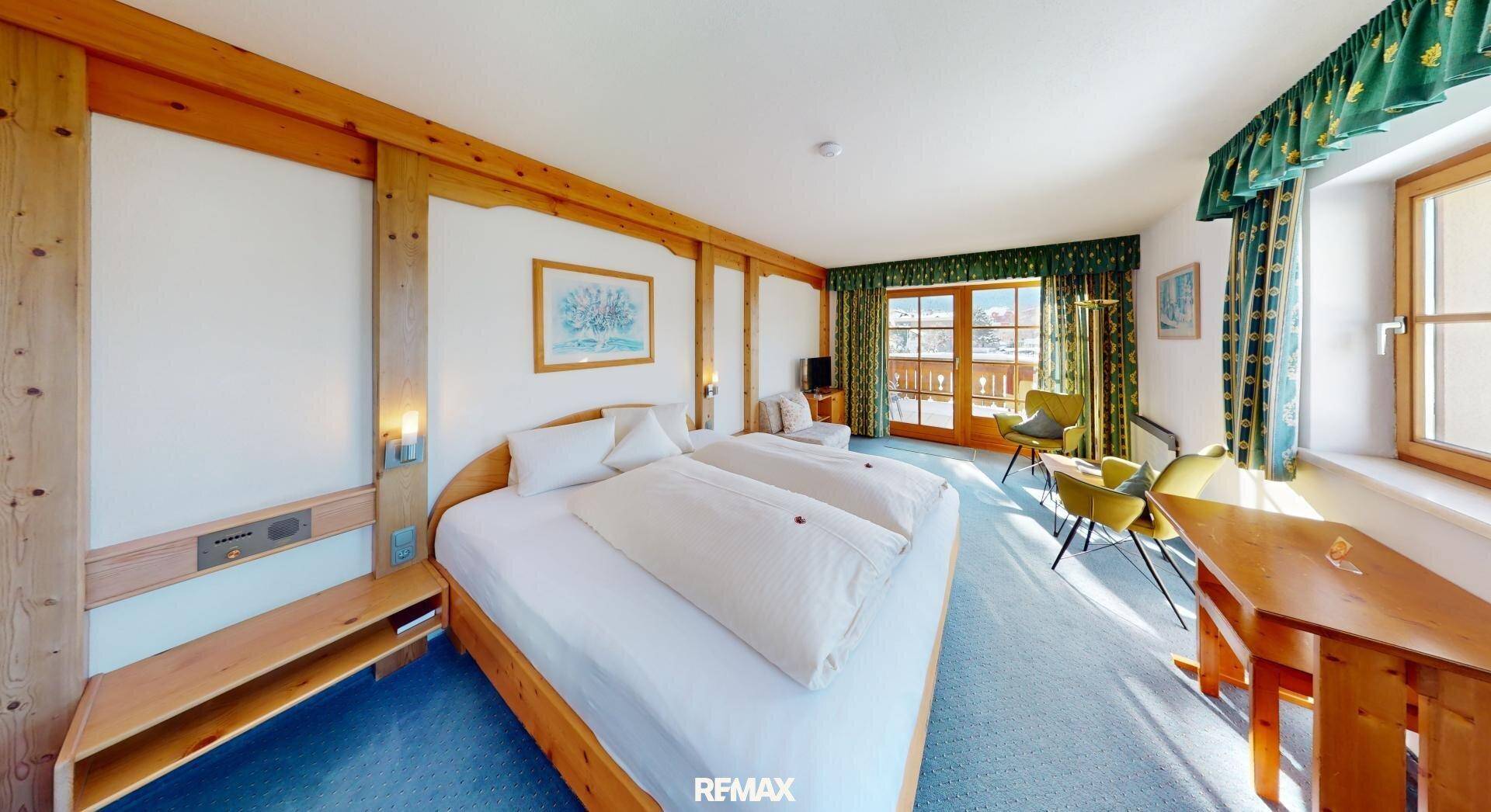 Helles Schlafzimmer mit Holzbett, blauem Teppich und Zugang zu einem Balkon mit Bergblick.