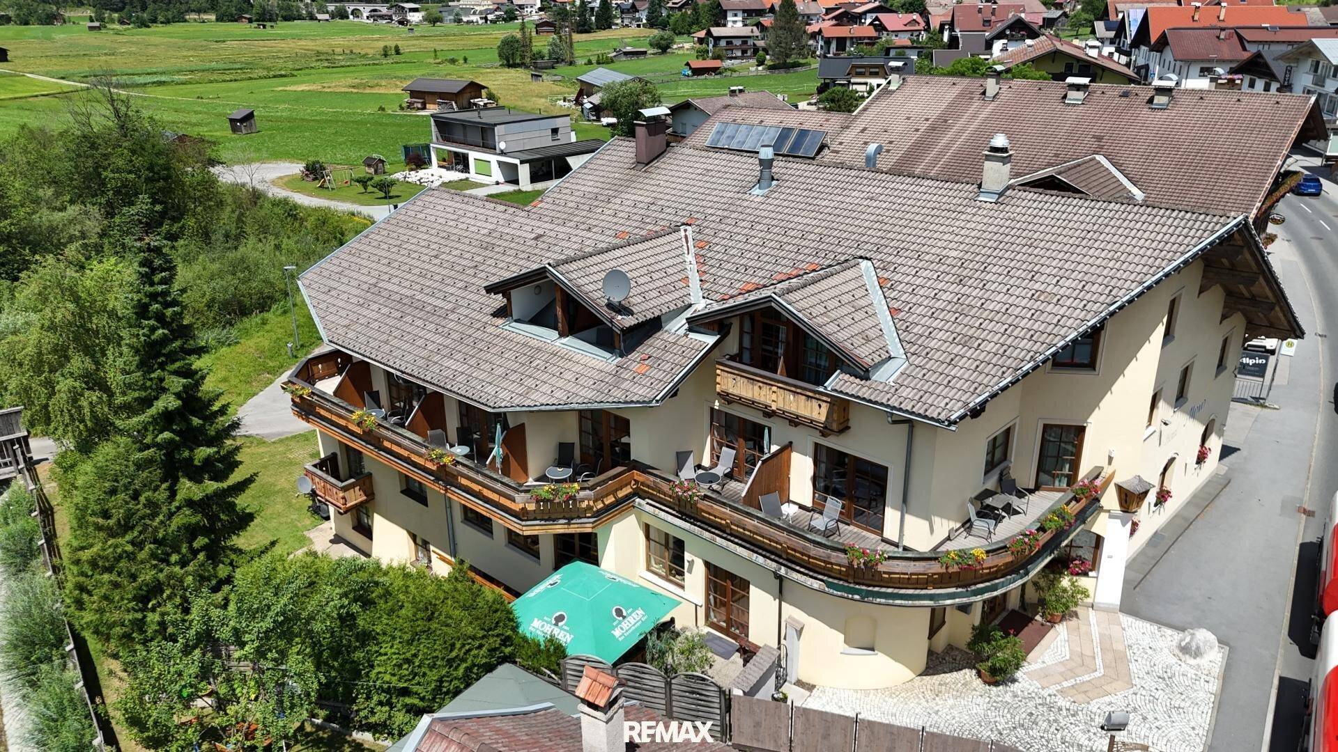 Luftaufnahme eines großen Gebäudes mit mehreren Balkonen und einem Satteldach in grüner Umgebung.