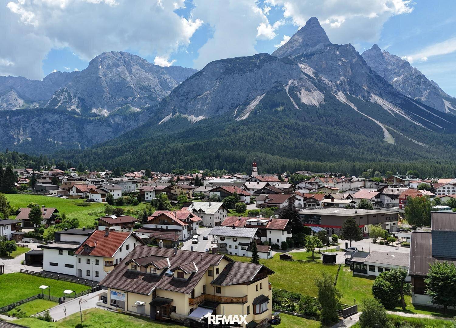Malerische Berglandschaft mit einem Dorf im Tal, umgeben von grünen Wiesen und hohen Gipfeln.