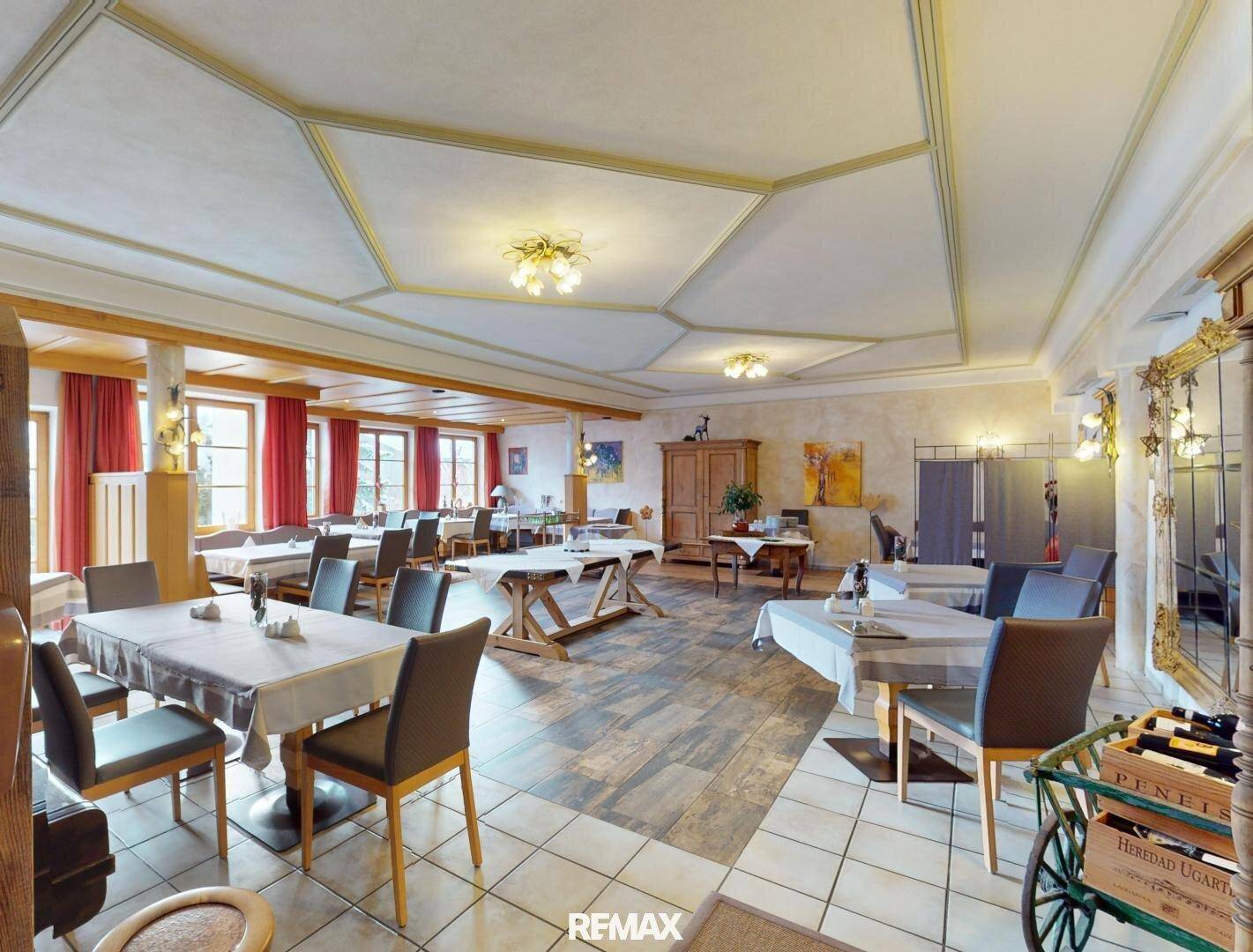 Geräumiger Speisesaal mit mehreren Tischen, modernen Stühlen und einer strukturierten Decke.