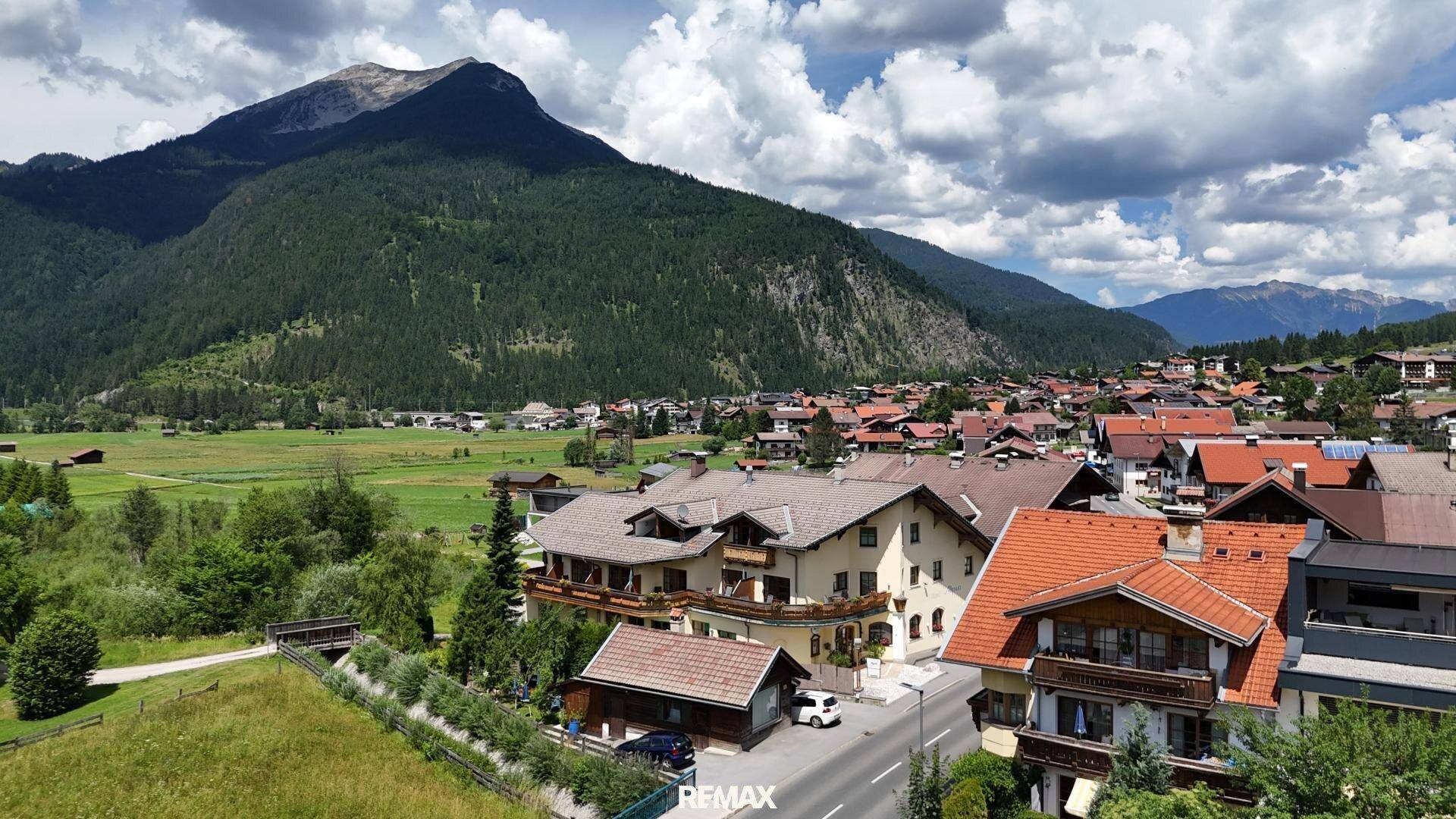 Dorfansicht mit traditionellen Häusern, umgeben von grünen Hügeln und einer beeindruckenden Bergkulisse.