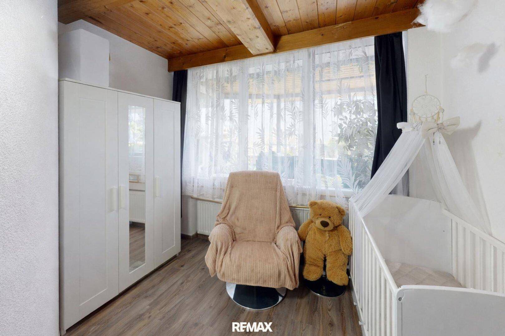 Helles Kinderzimmer mit Holzbalkendecke, Laminatboden und großem Fenster.