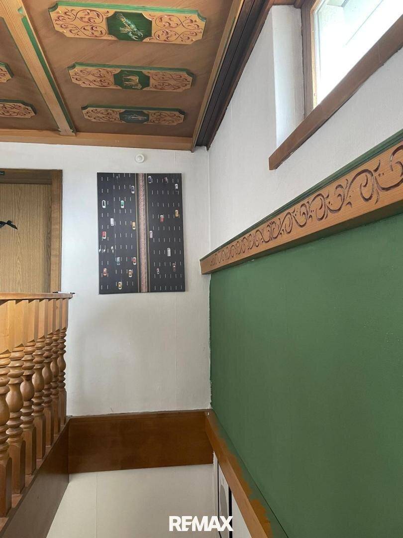 Treppenhaus mit grüner Wand, Holzgeländer und dekorativer Holzdecke.