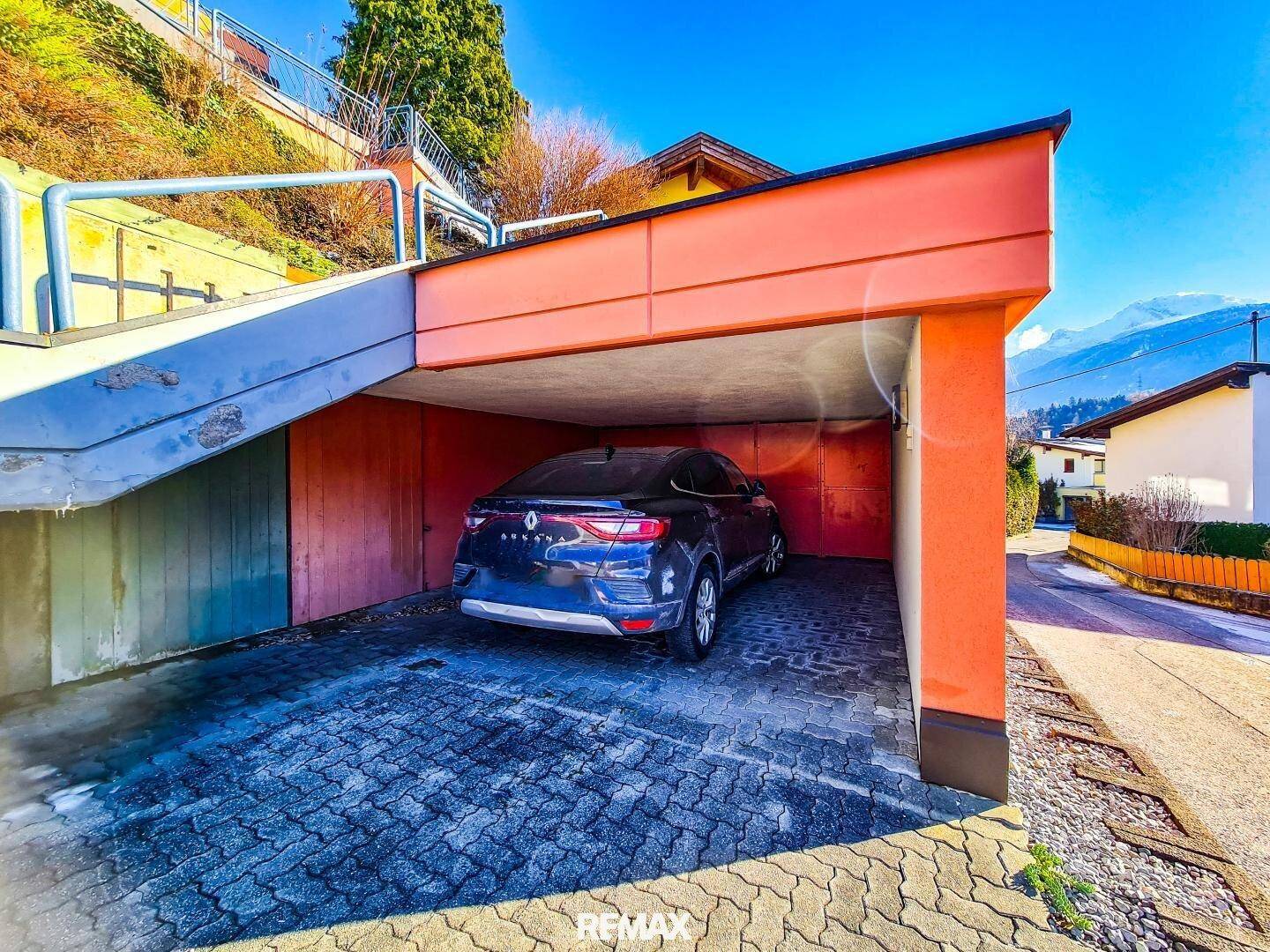 Überdachter Stellplatz für ein Auto vor einem Wohnhaus in Hanglage.